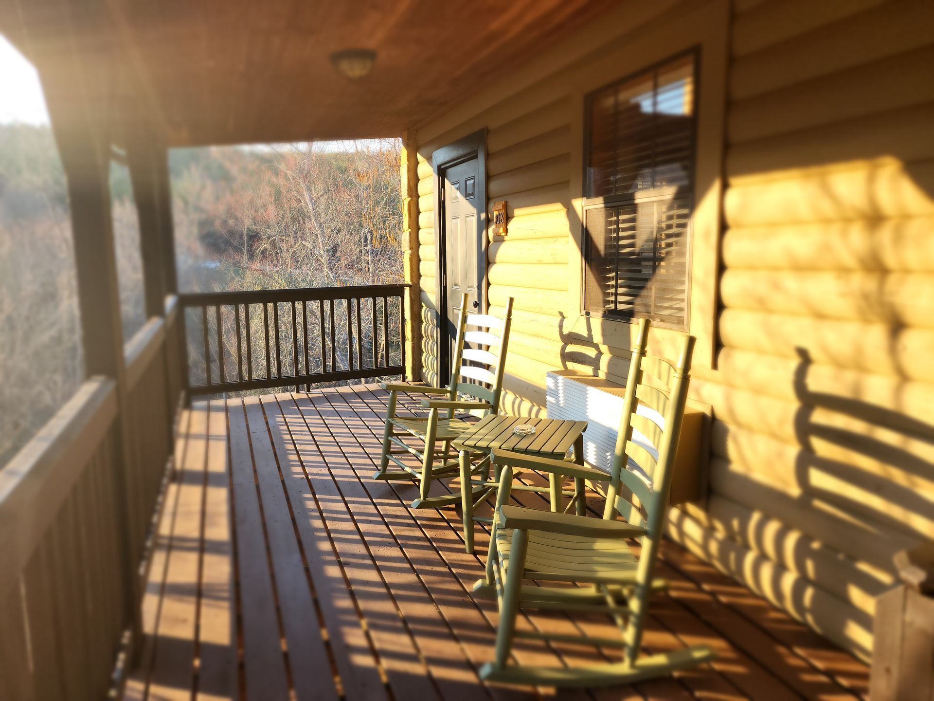 Wooden porch with rocking chairs overlooking a landscape, bathed in warm sunlight.