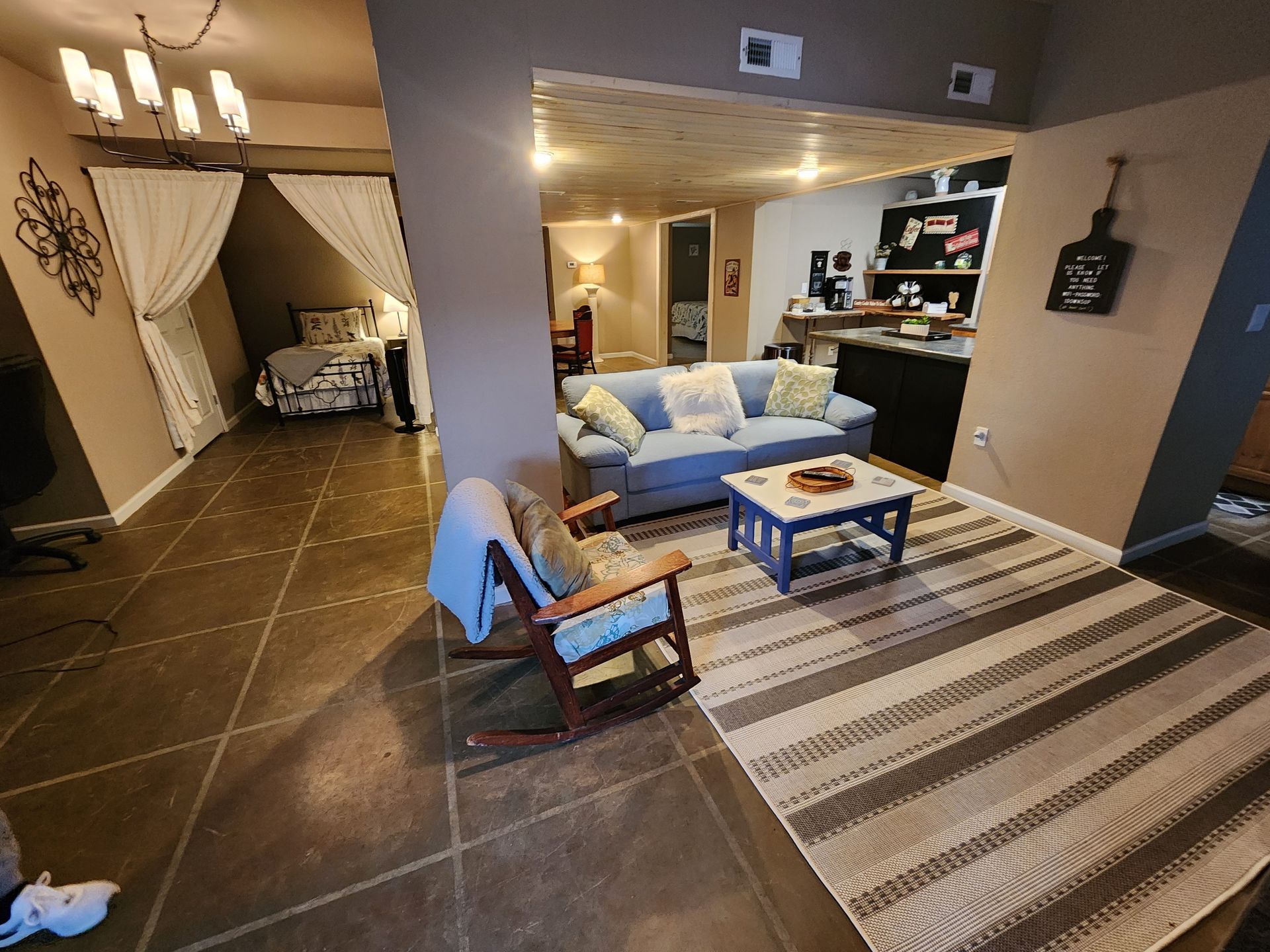 Open-concept living space with bedroom, living room, and kitchen. Includes sofa, rocking chair, rug, and coffee table.
