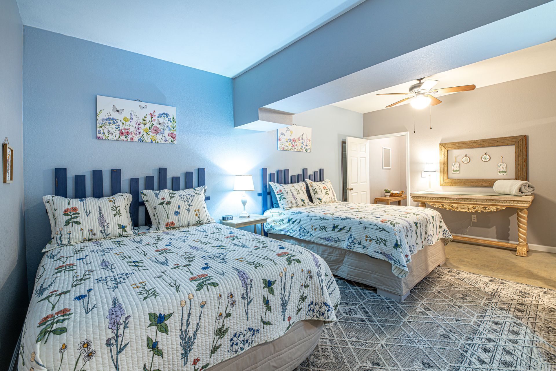Bedroom with two beds, floral bedding, blue walls, wooden headboards, and a rug.
