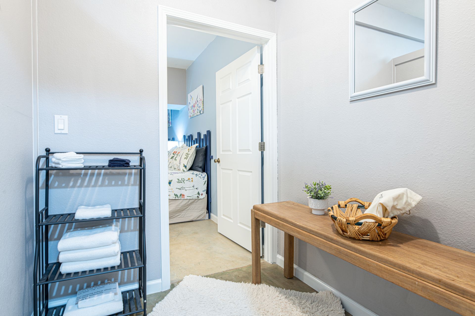 Hallway with shelf of towels, wooden bench, and open bedroom door.