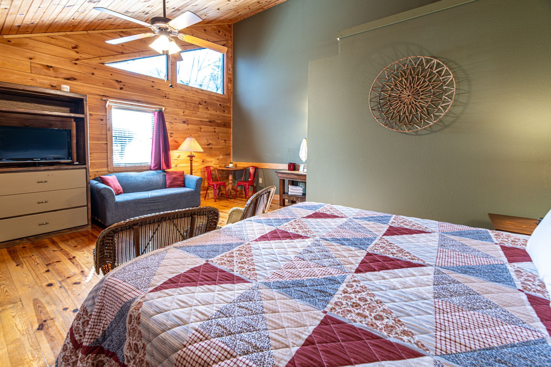 Bedroom with wooden walls and ceiling, queen bed with quilt, sofa, and television.