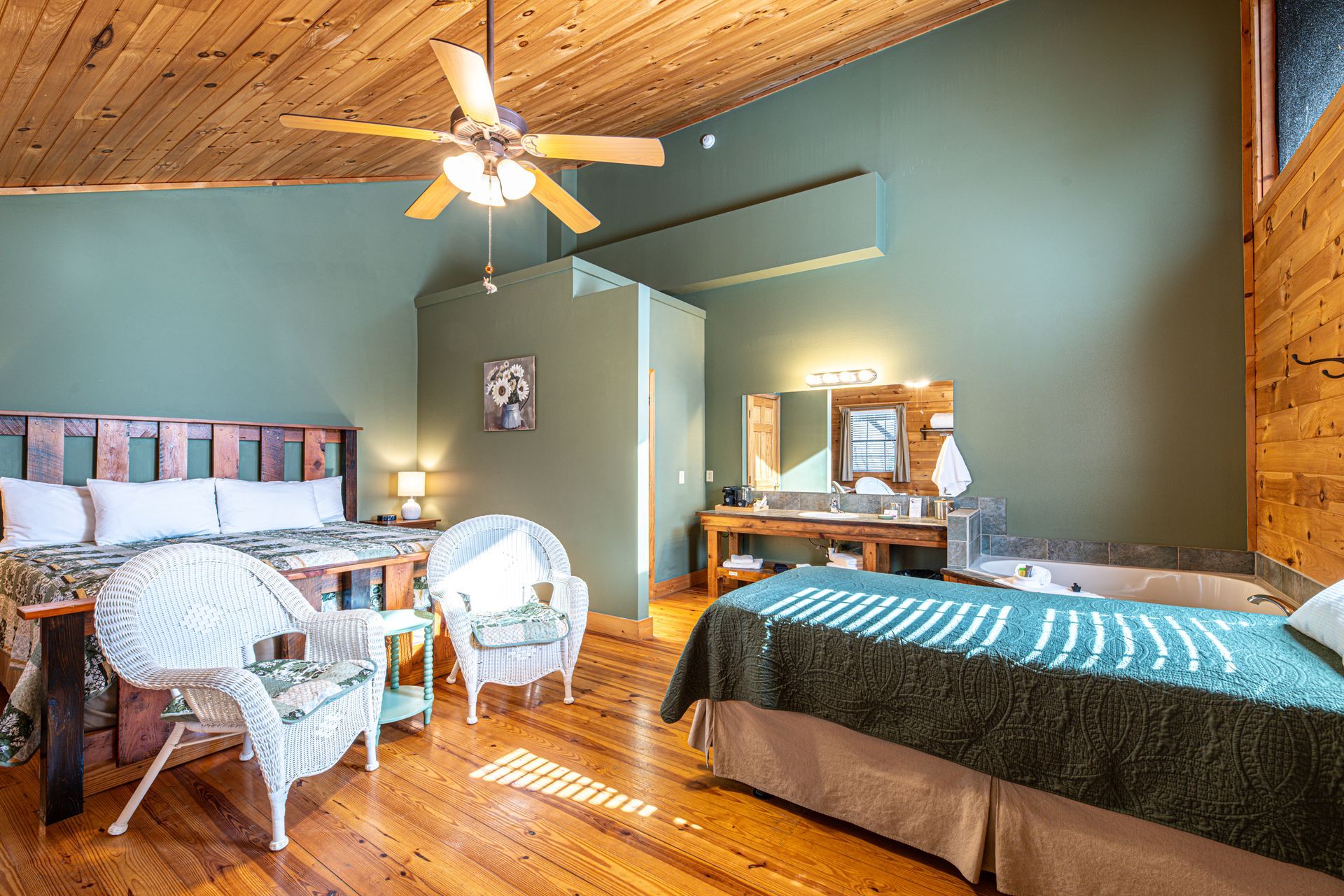 Spacious bedroom with wooden ceiling and floor, large bed, two white wicker chairs, and a vanity.