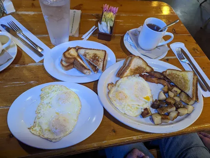 Breakfast meal: eggs, toast, potatoes, bacon, and tea on a wooden table.