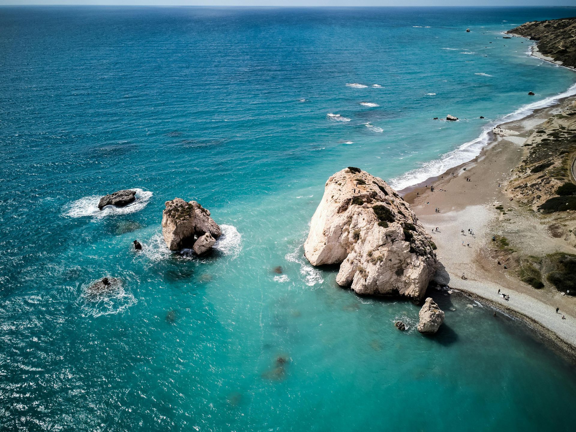 Turquoise ocean with rocky shoreline and sandy beach under clear sky