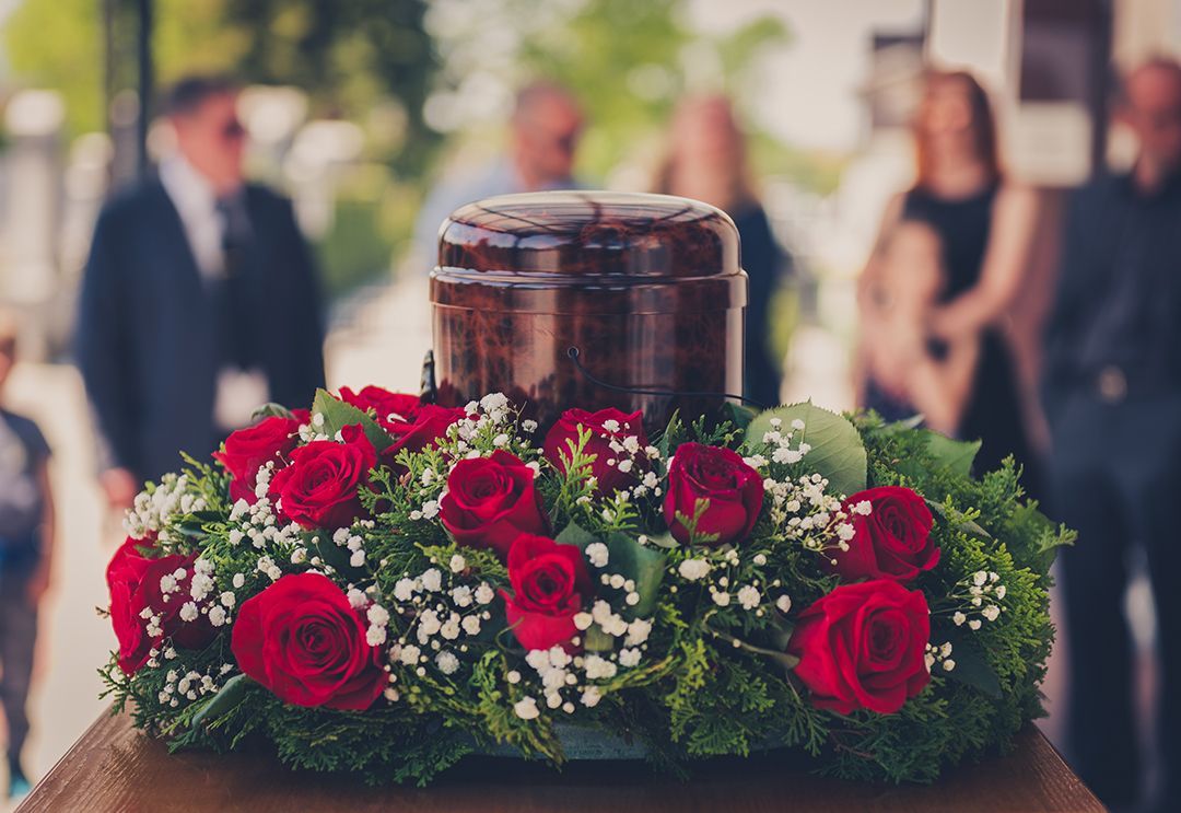 A urn surrounded by red roses and baby 's breath is on a coffin at a funeral.