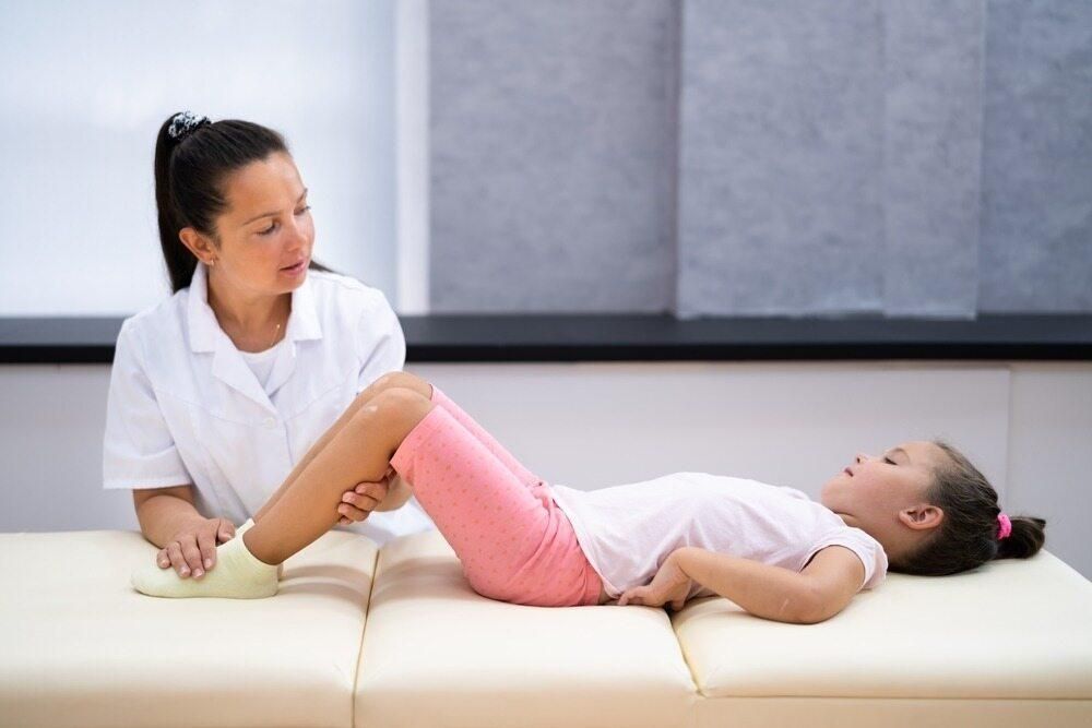 A Young Girl Is Laying On A Bed While A Nurse Examines Her Leg — Trinity Family Chiropractic In Brinsmead, QLD