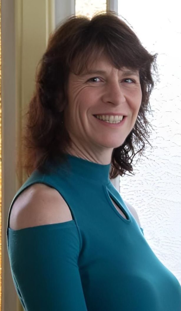 A Woman In A Blue Shirt Is Smiling In Front Of A Window — Trinity Family Chiropractic In Cairns, QLD
