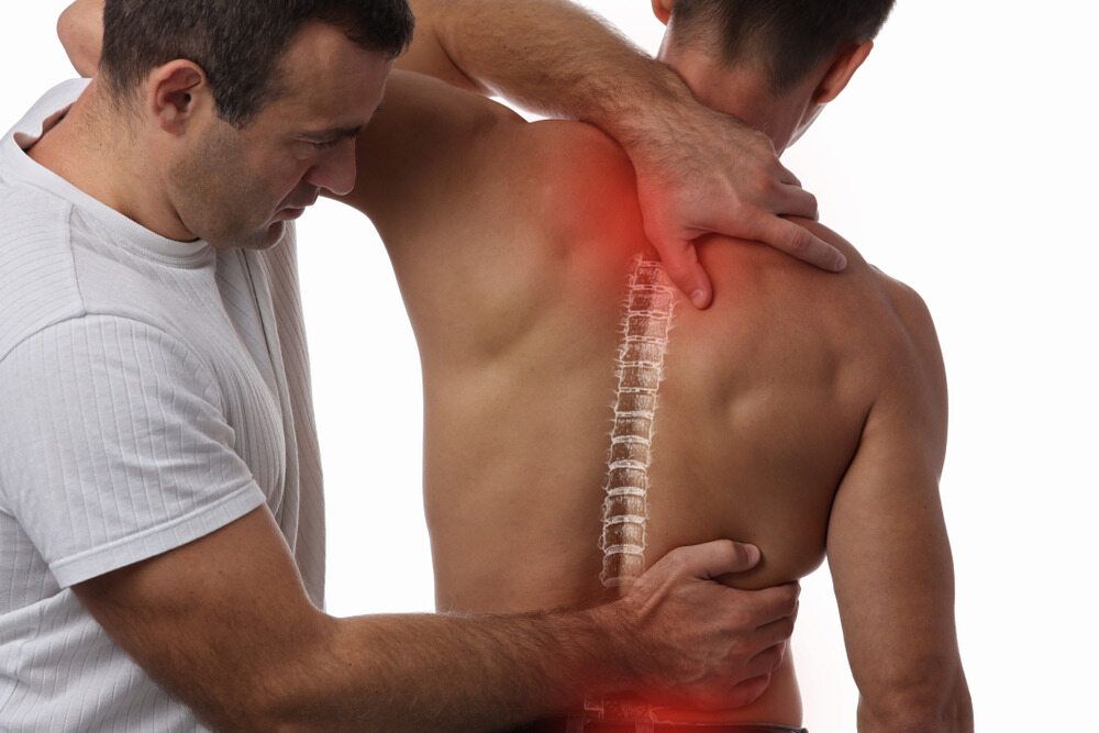 A Man Is Giving A Back Massage To Another Man — Trinity Family Chiropractic In Cairns, QLD