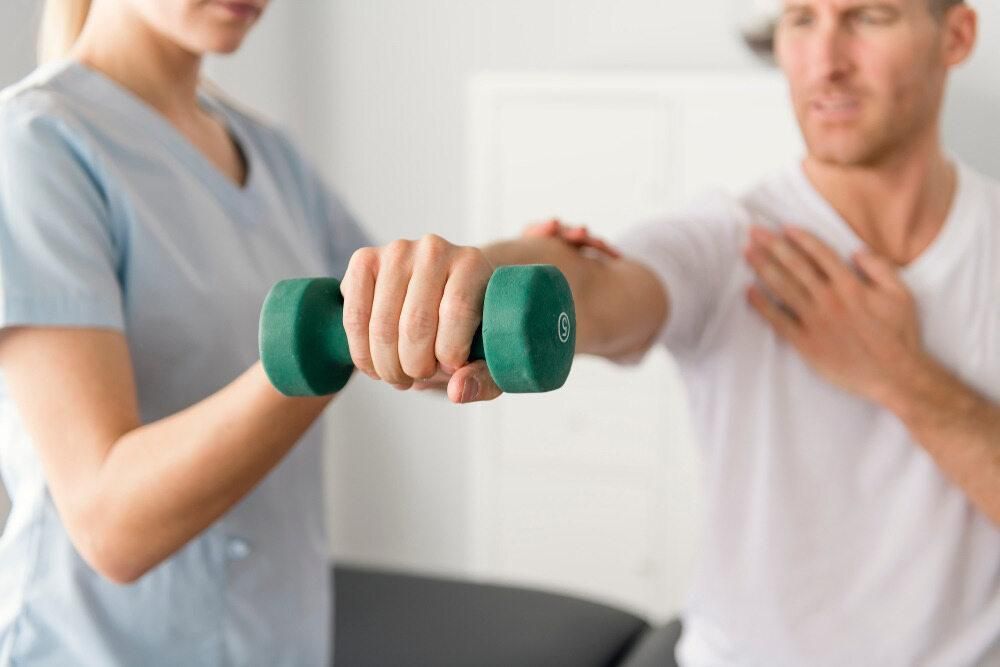 A Woman Is Helping A Man Lift A Green Dumbbell — Trinity Family Chiropractic In North Cairns, QLD