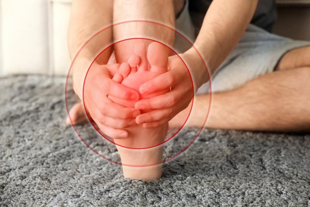 A Person Is Sitting On The Floor Holding Their Foot In Pain — Trinity Family Chiropractic In Parramatta Park, QLD