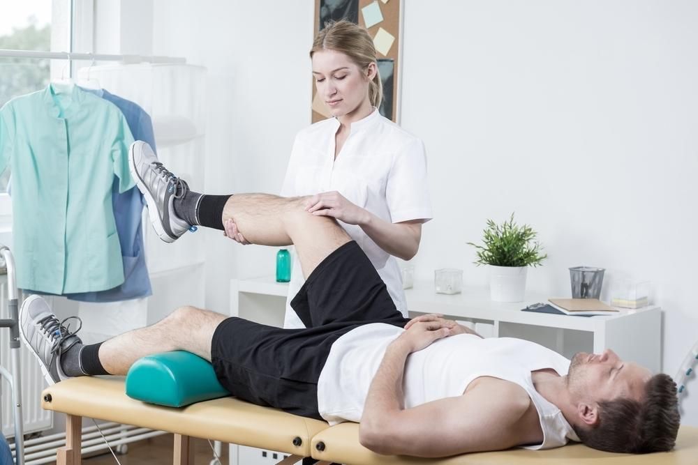 A Man Is Laying On A Table While A Woman Stretches His Leg — Trinity Family Chiropractic In Smithfield, QLD