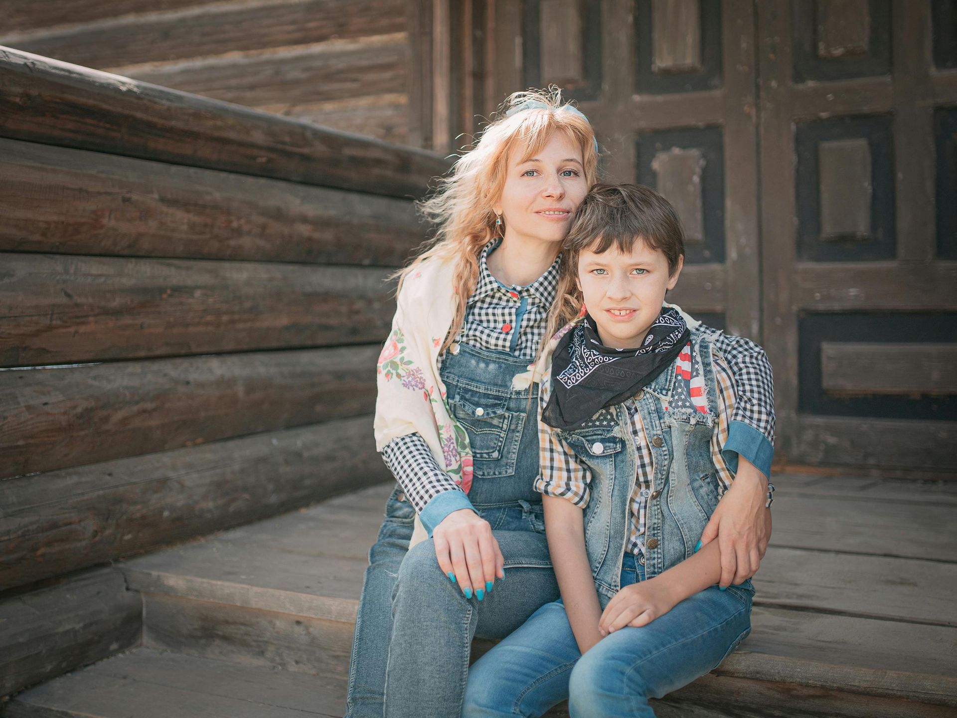 A woman and a boy are sitting on the steps of a log cabin.