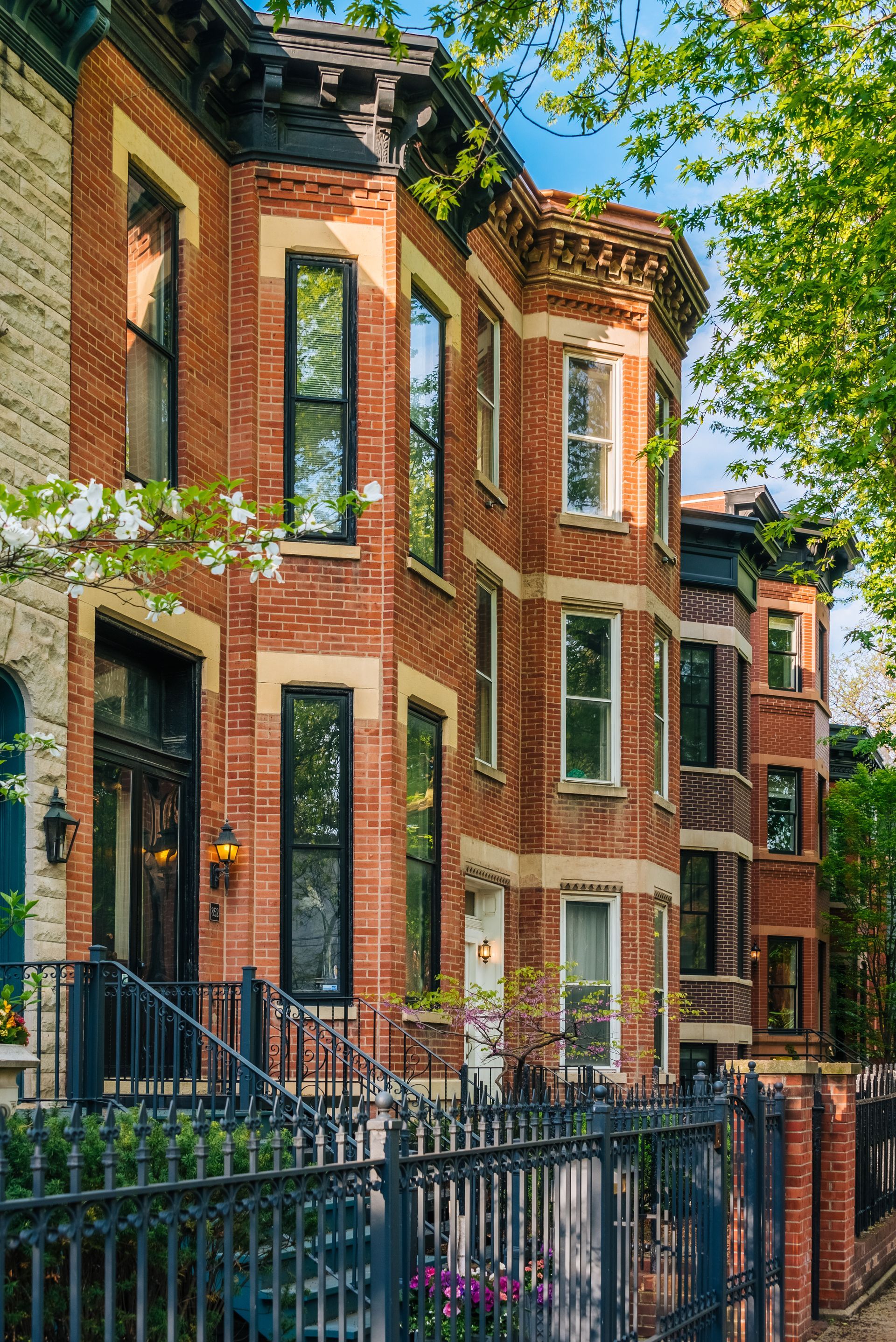 Red brick rowhouses with tall windows and black iron fences on a leafy city street