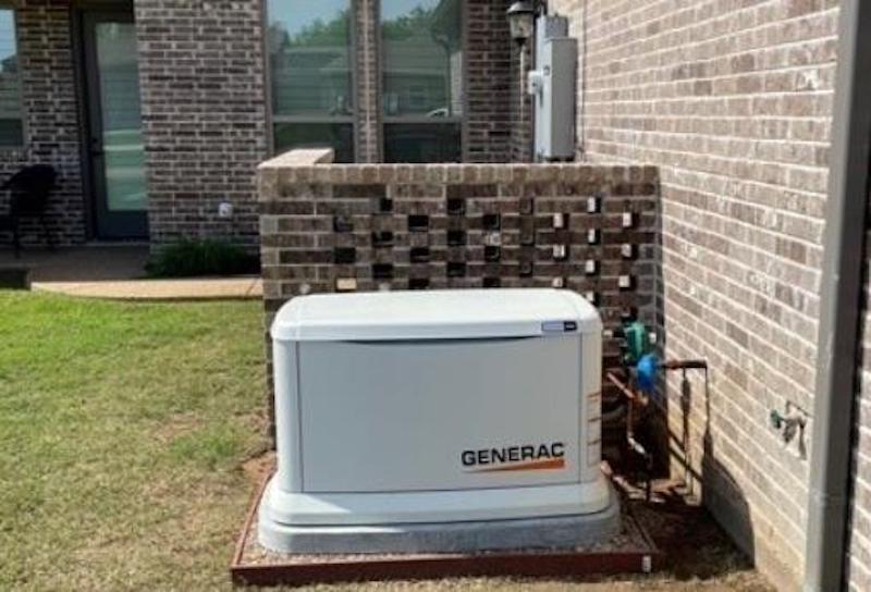 A generator is sitting on the side of a brick building.