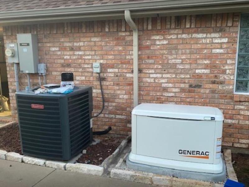 A generator is sitting next to an air conditioner on the side of a brick house.