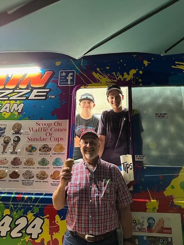 Two smiling people posing inside a colorful photo booth with menu graphics and a large glass panel