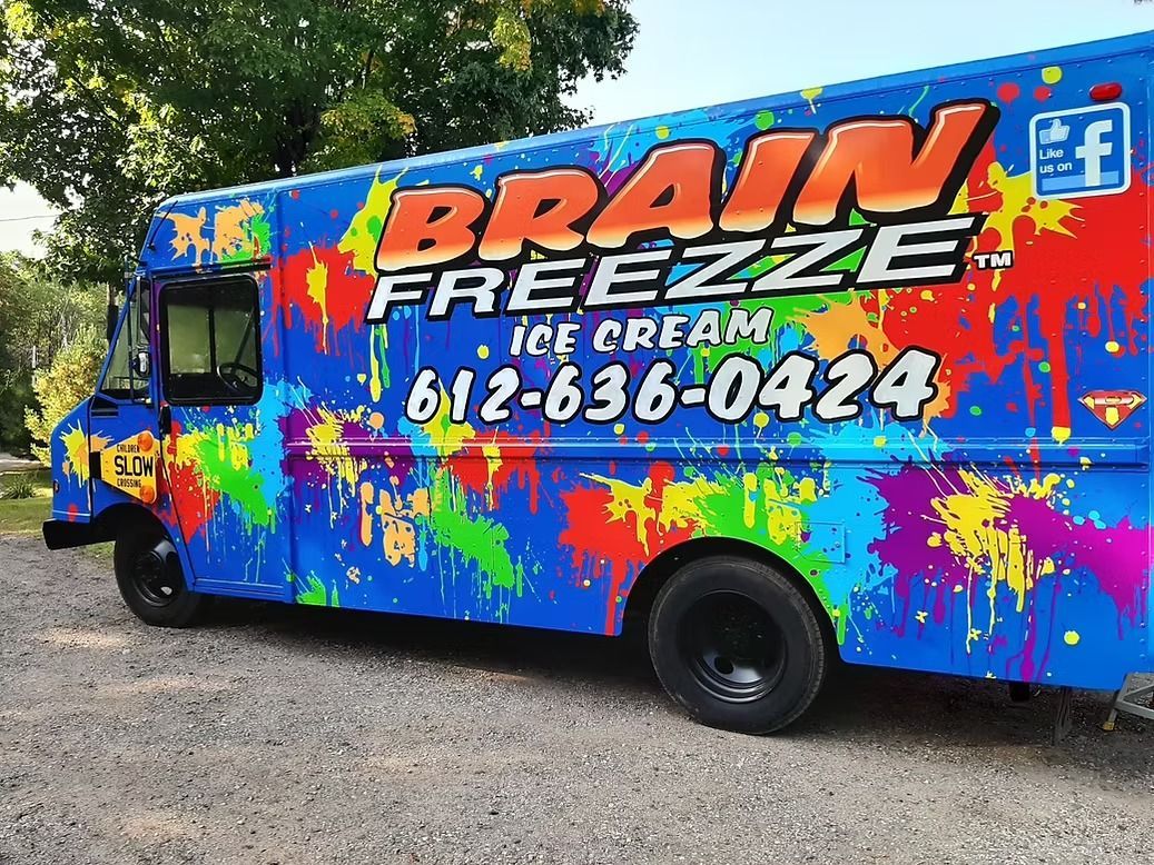 Colorful Brain Freeze ice cream truck parked on a gravel roadside, with trees in the background.