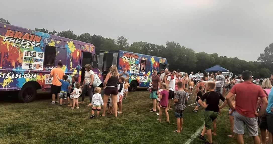 Crowd gathered outdoors near colorful decorated food trucks at a festival on a grassy field