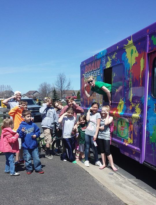Children posing beside a colorful purple bus mural with a person leaning out, outdoors on a sunny day