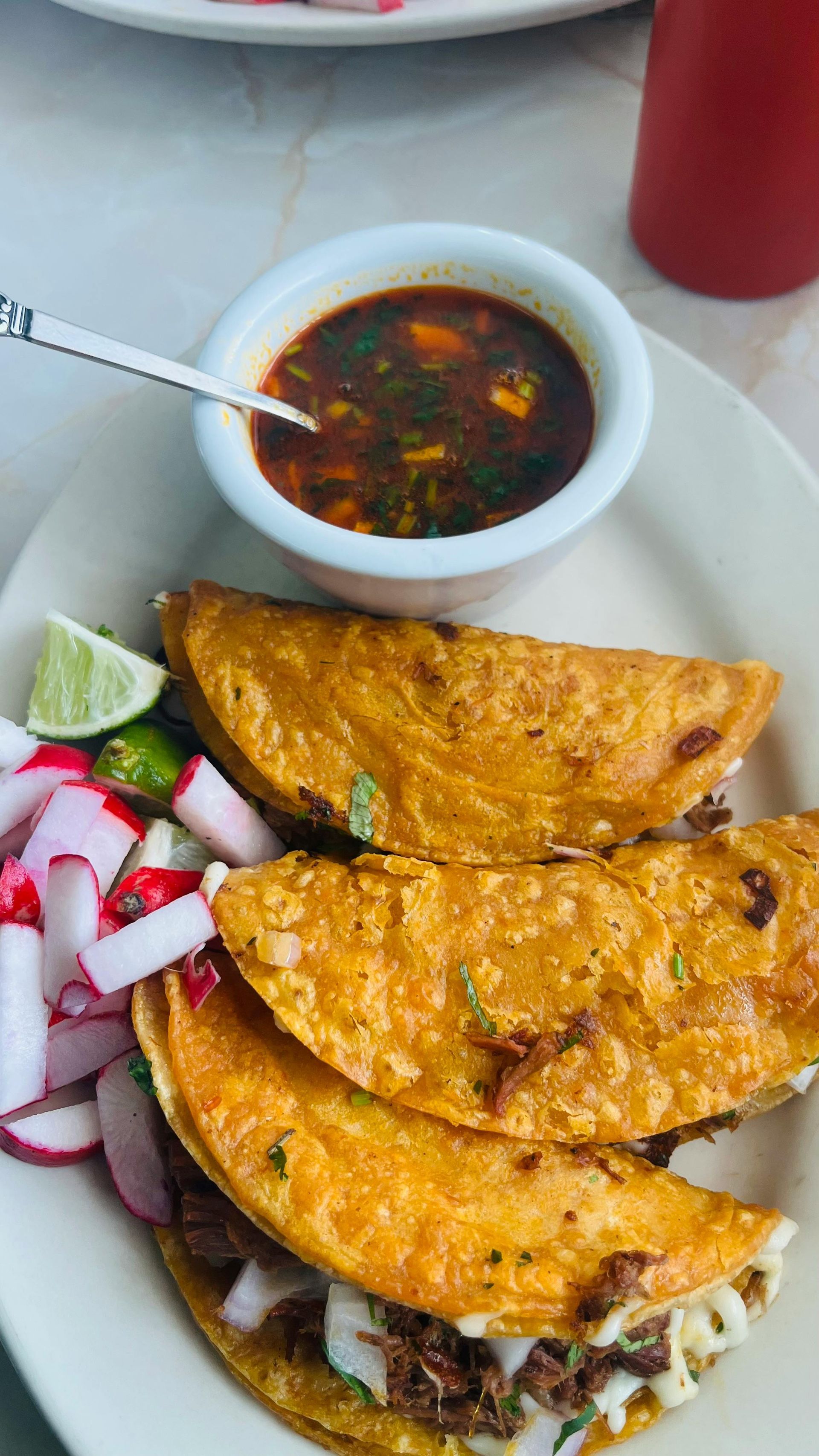 A white plate topped with tacos and a bowl of sauce.