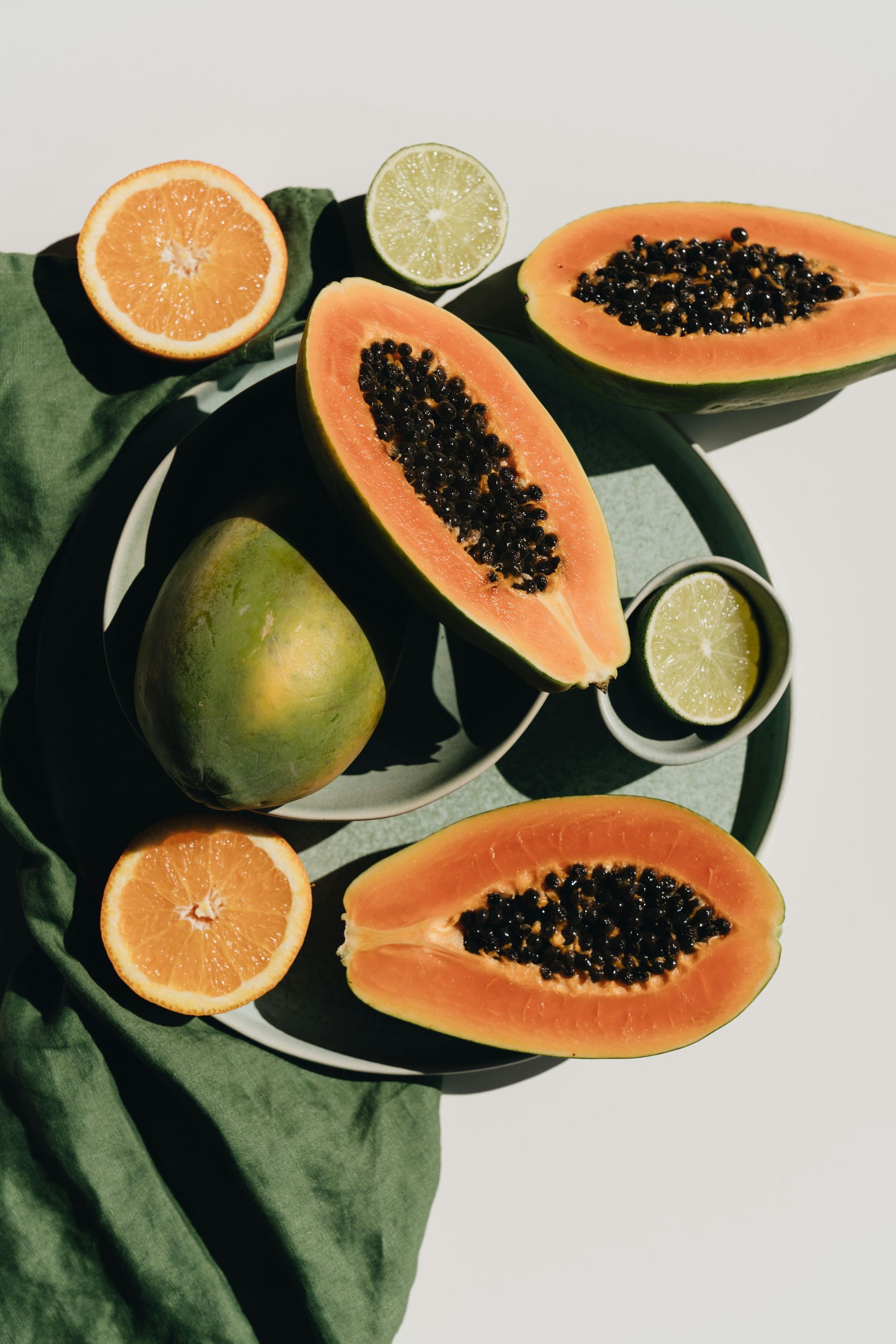 A bowl of papaya , oranges , limes and mangoes on a table.