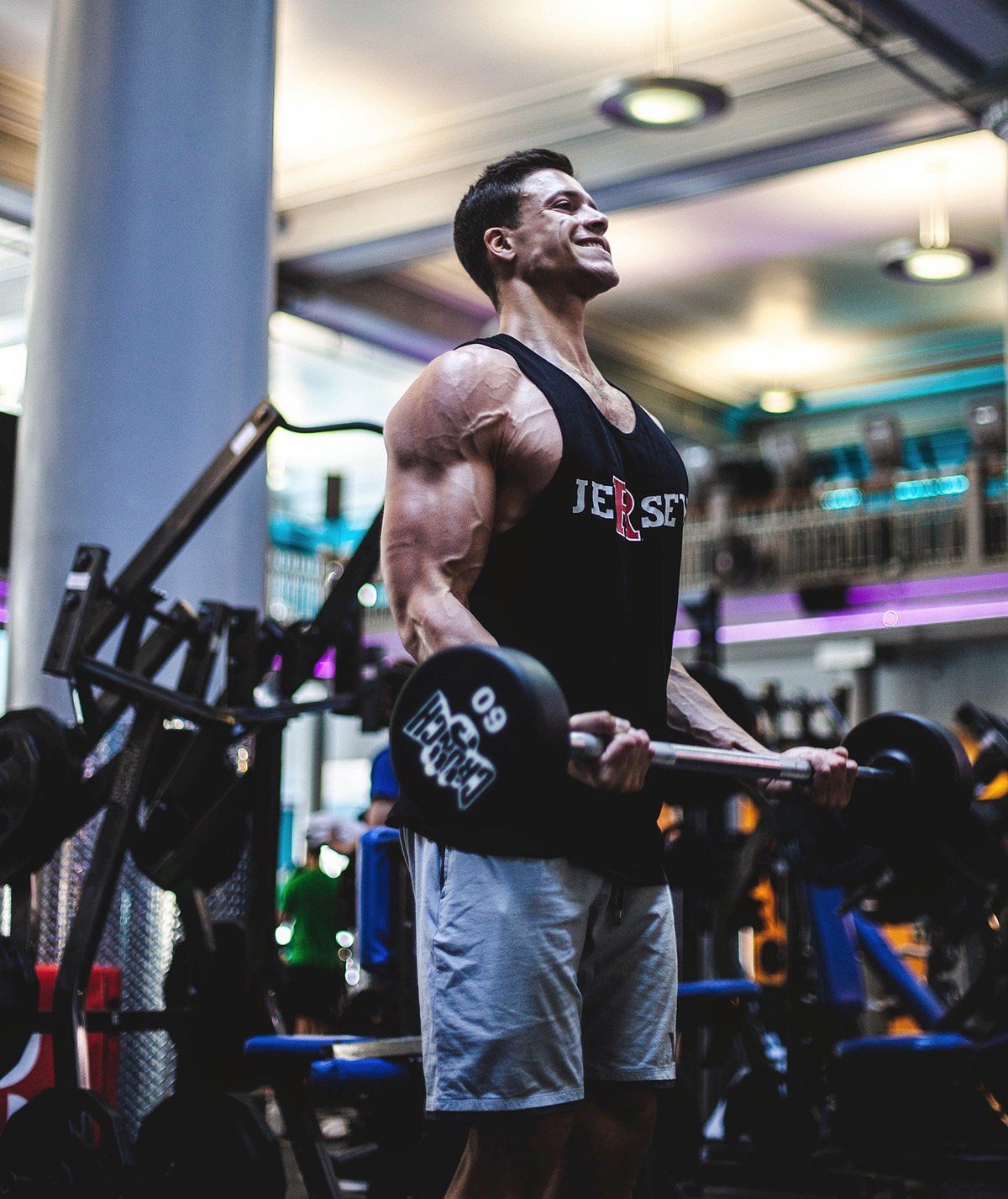 A man in a black tank top is lifting a barbell in a gym.