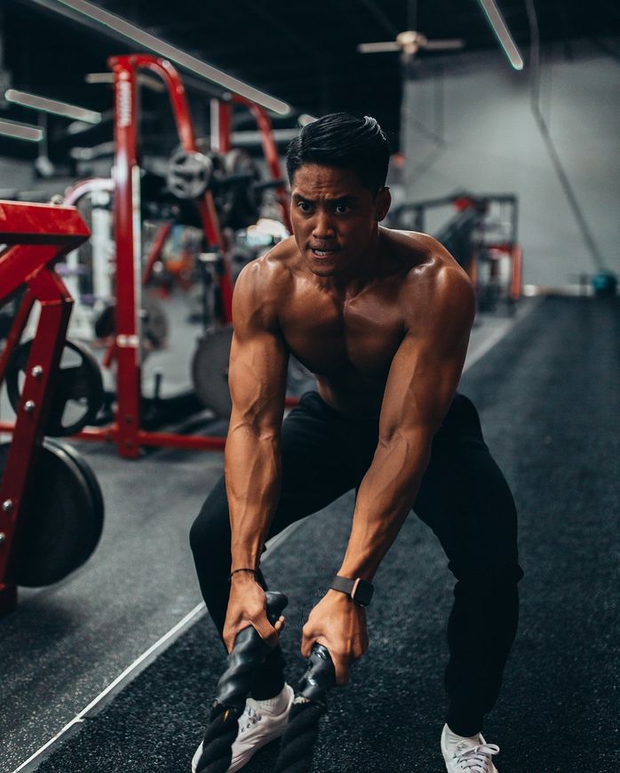 A shirtless man is lifting a barbell in a gym.