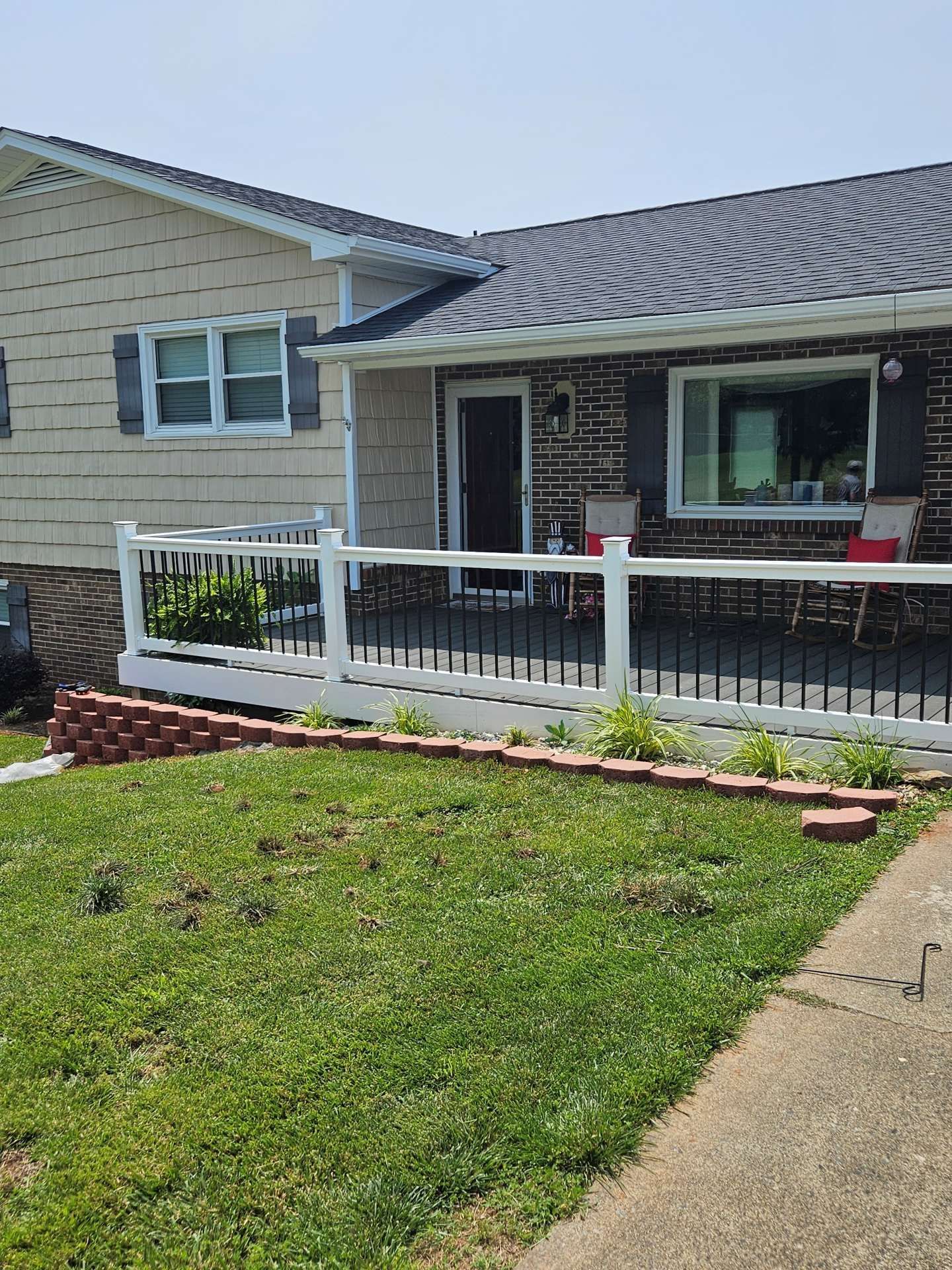 Single-story house with a white railing porch and green front lawn on a sunny day