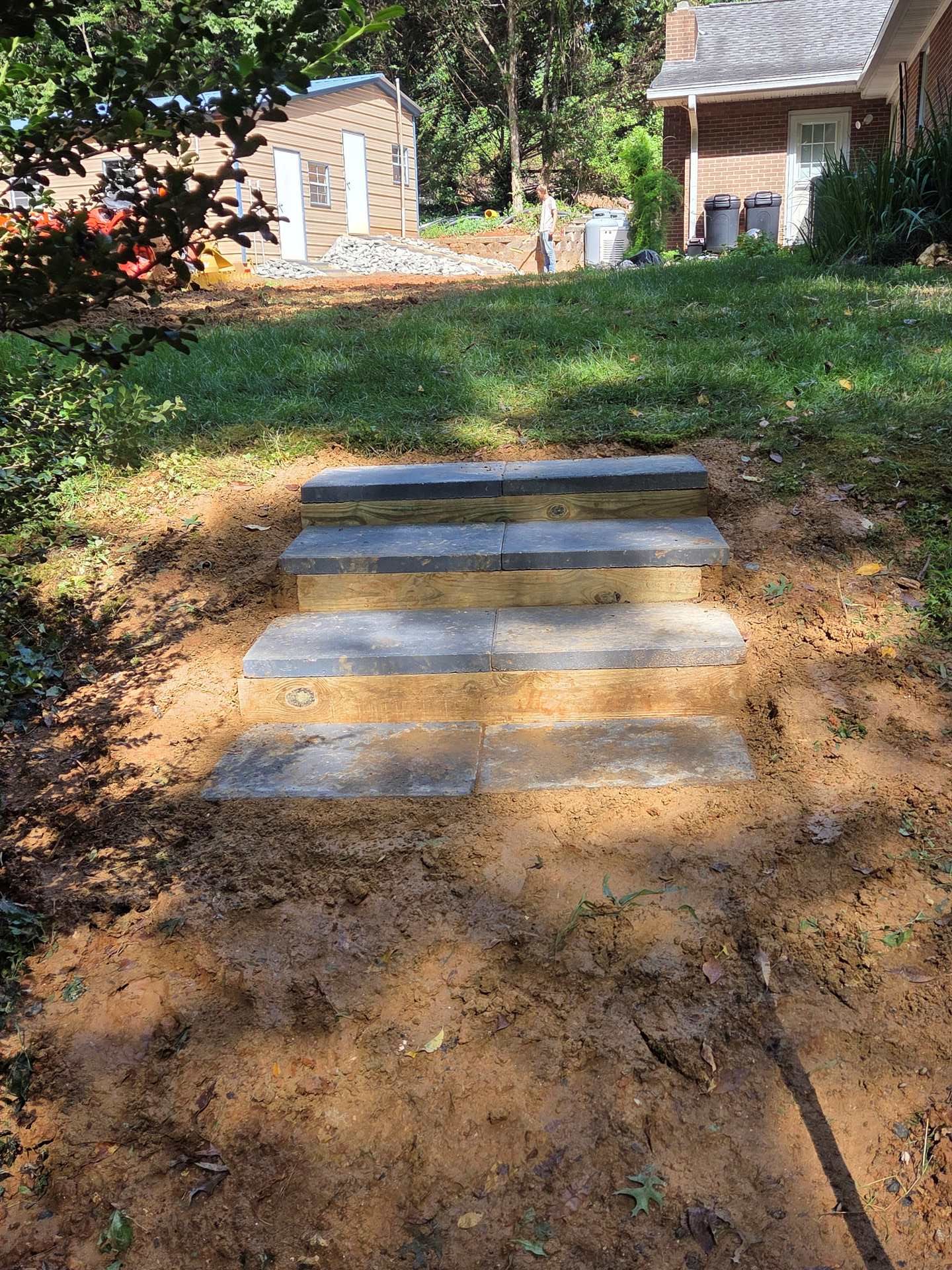 Short concrete steps on a dirt path leading up to a grassy yard with houses in the background