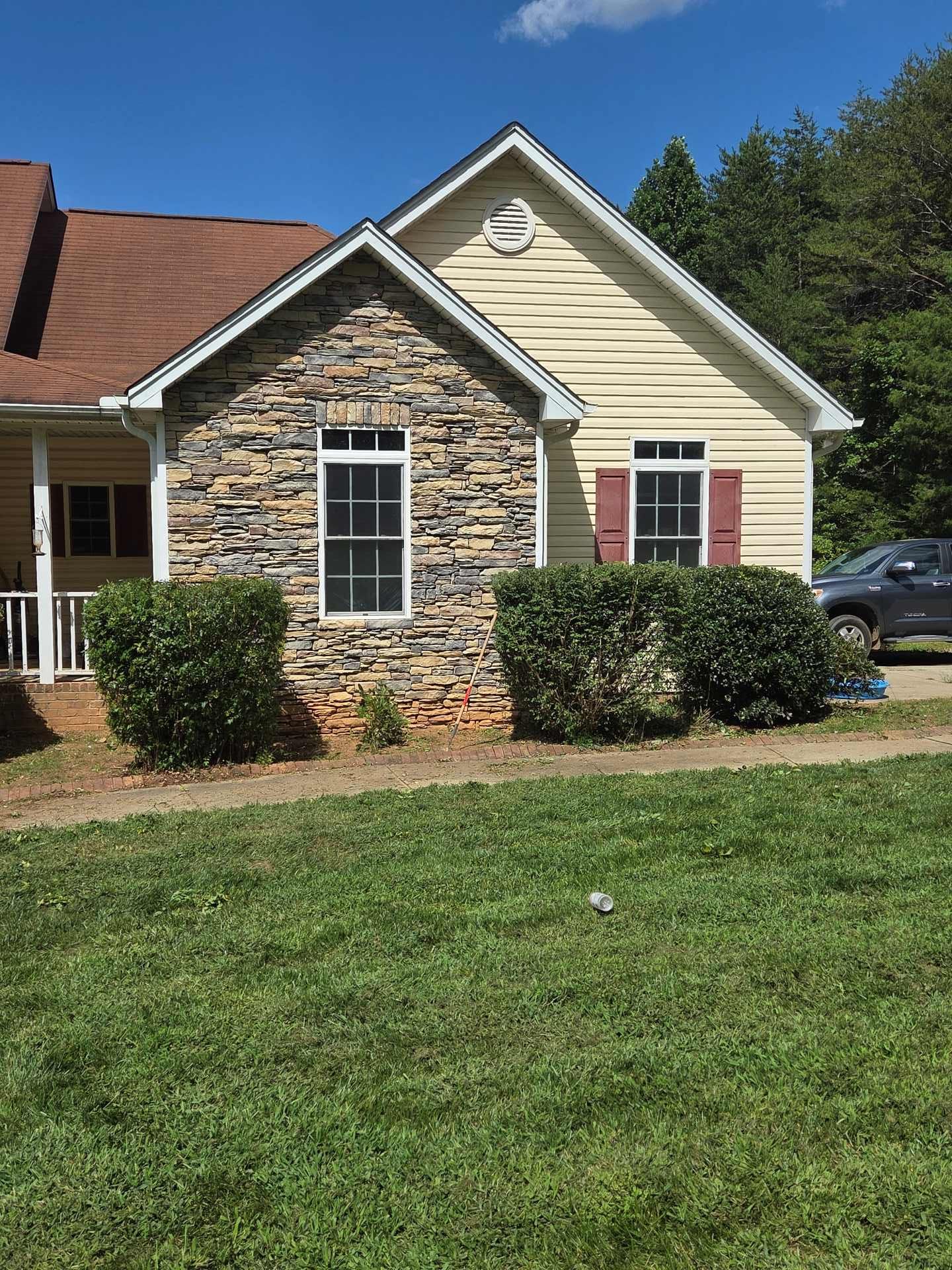 Suburban house with stone and beige siding, red shutters, and a green lawn in front