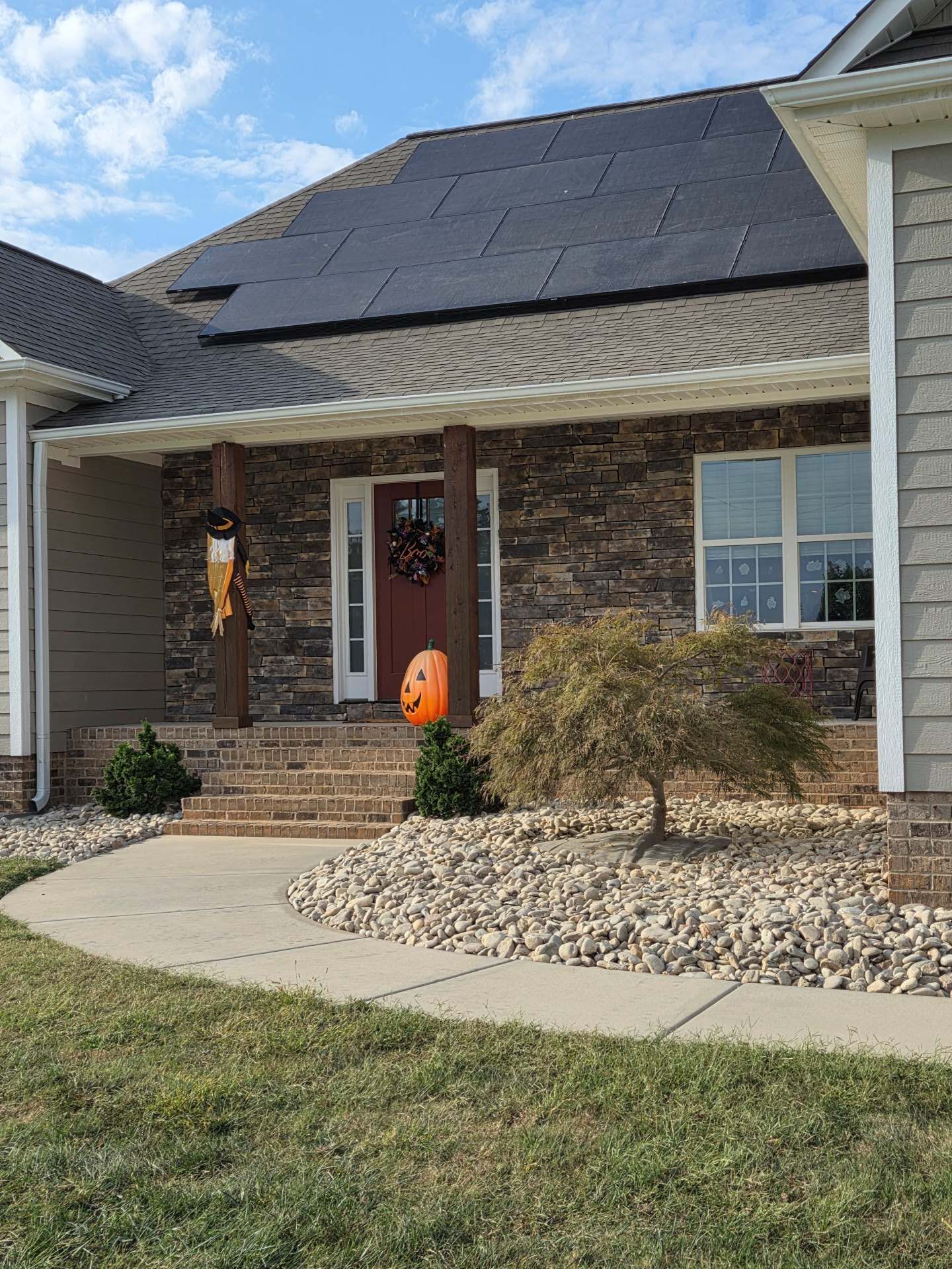 Suburban brick house with a solar-paneled roof, front porch, and Halloween pumpkin decoration