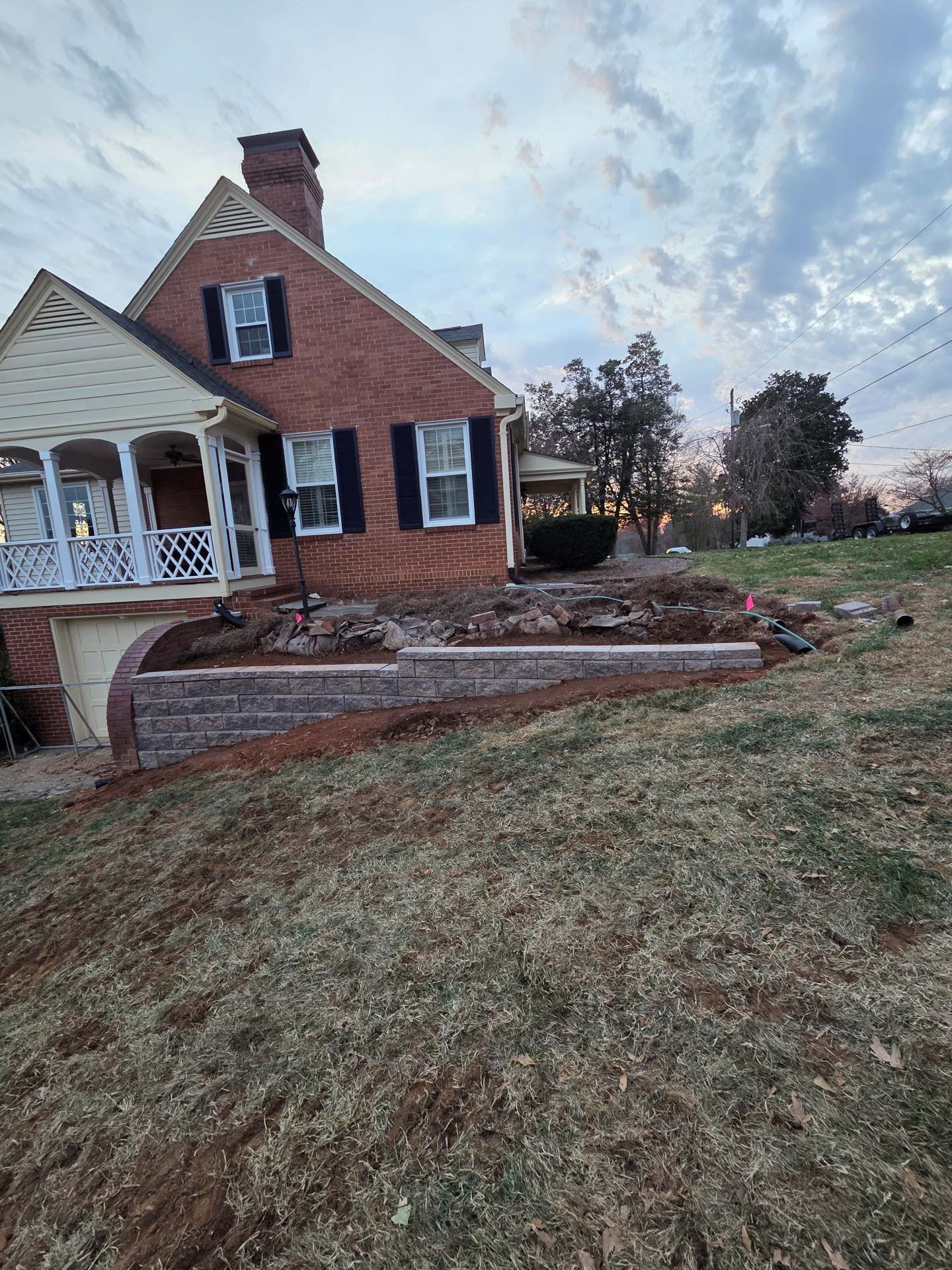 Brick house with white porch and chimney on a grassy hillside at dusk