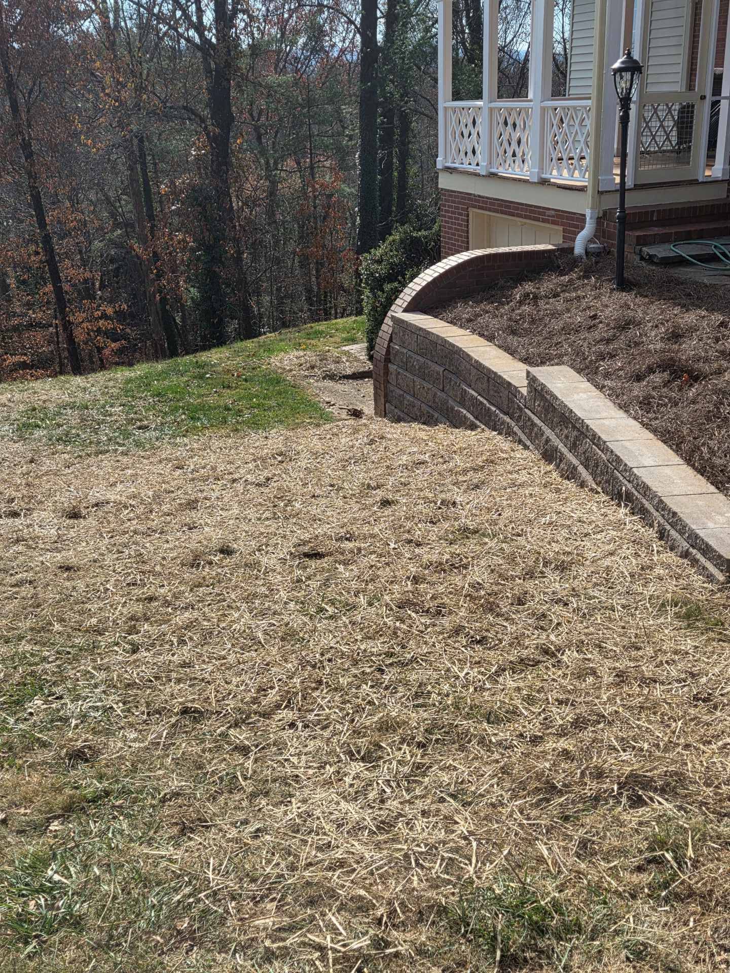 Curved stone retaining wall beside a house porch overlooking a sloped grassy yard and wooded area