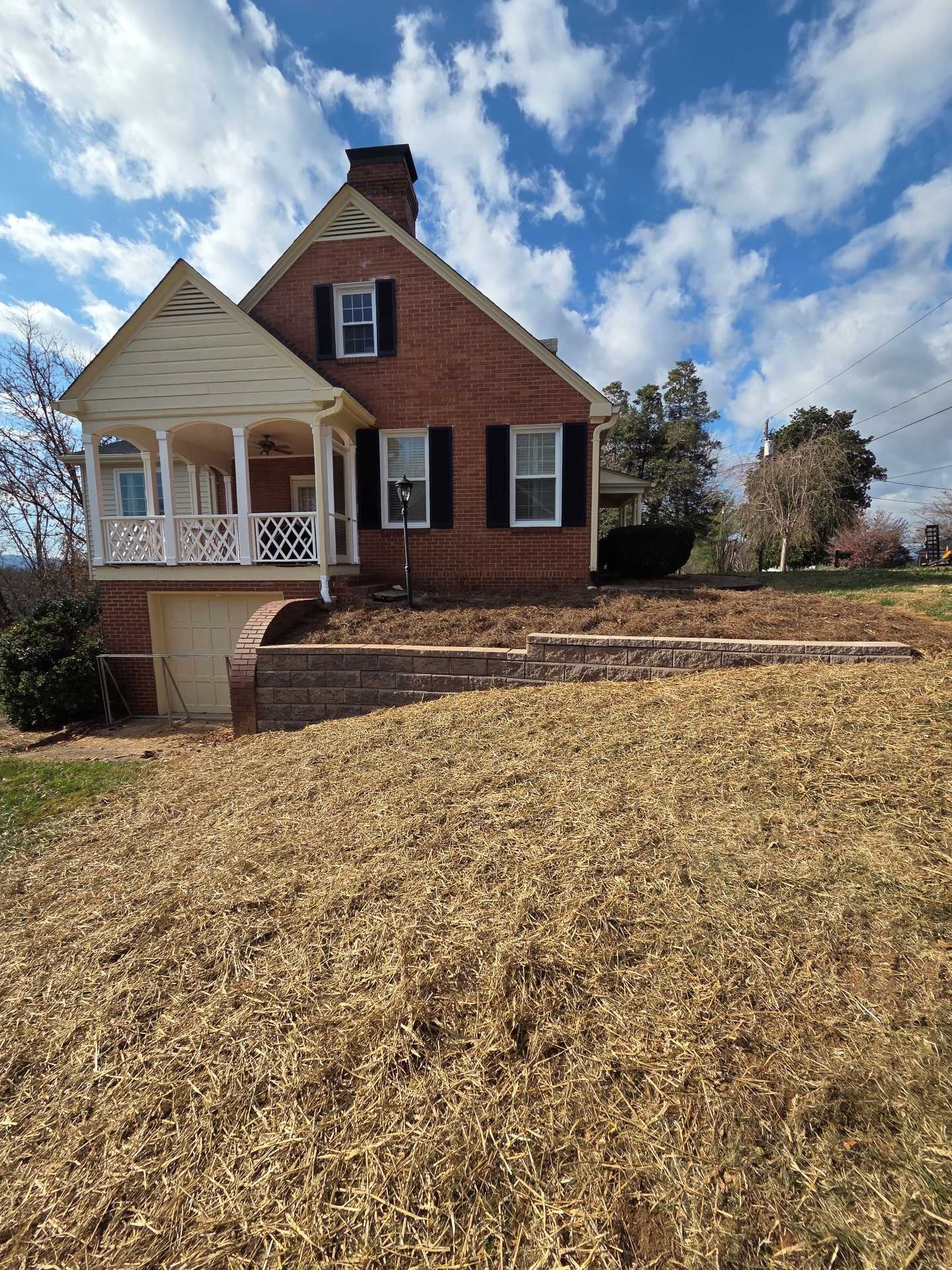 Brick house with white porch on a hill under a partly cloudy blue sky