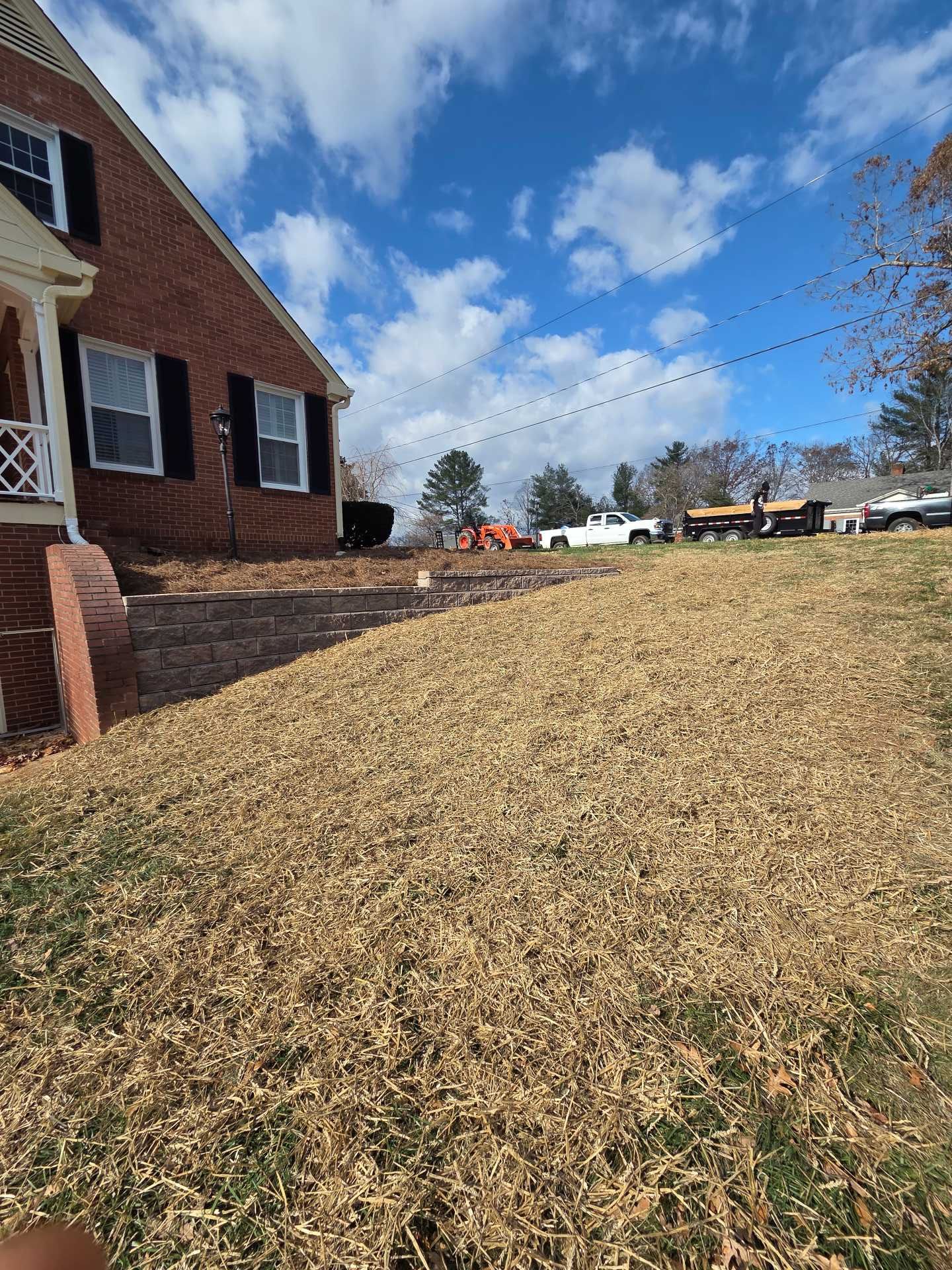 Brick house beside a sloped grassy lawn under a blue sky with scattered clouds