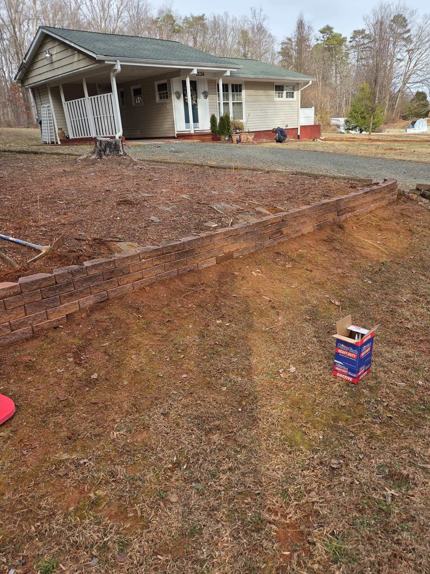 Rural house with a gravel driveway, dirt slope in foreground, and a small red-and-blue can near the bottom right.