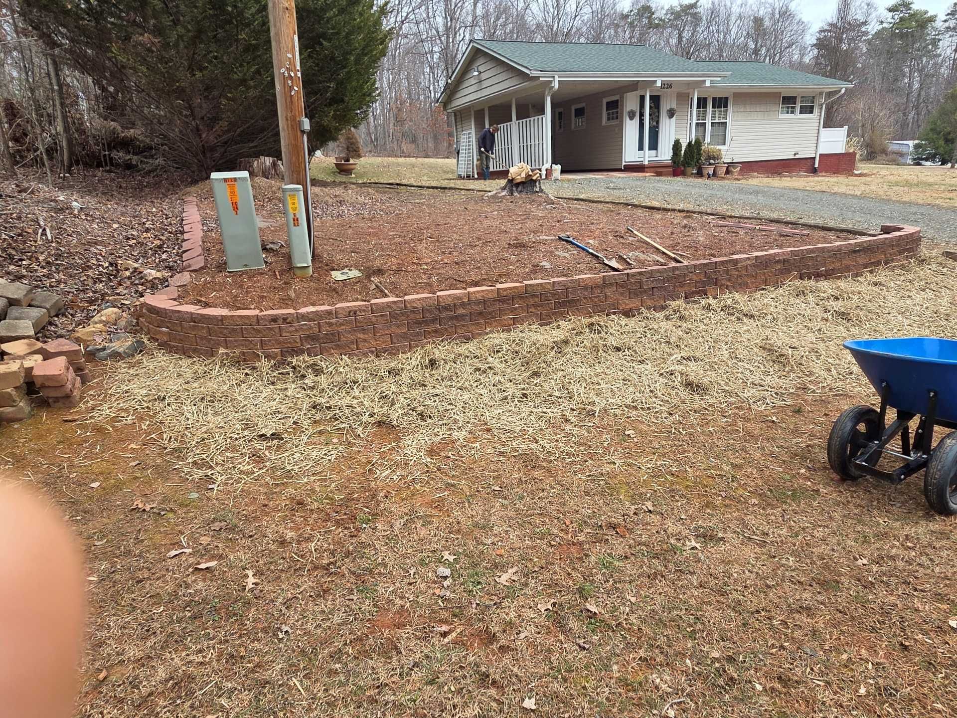 Gravel yard with a raised stone-edged bed, two utility boxes, and a small house in the background.