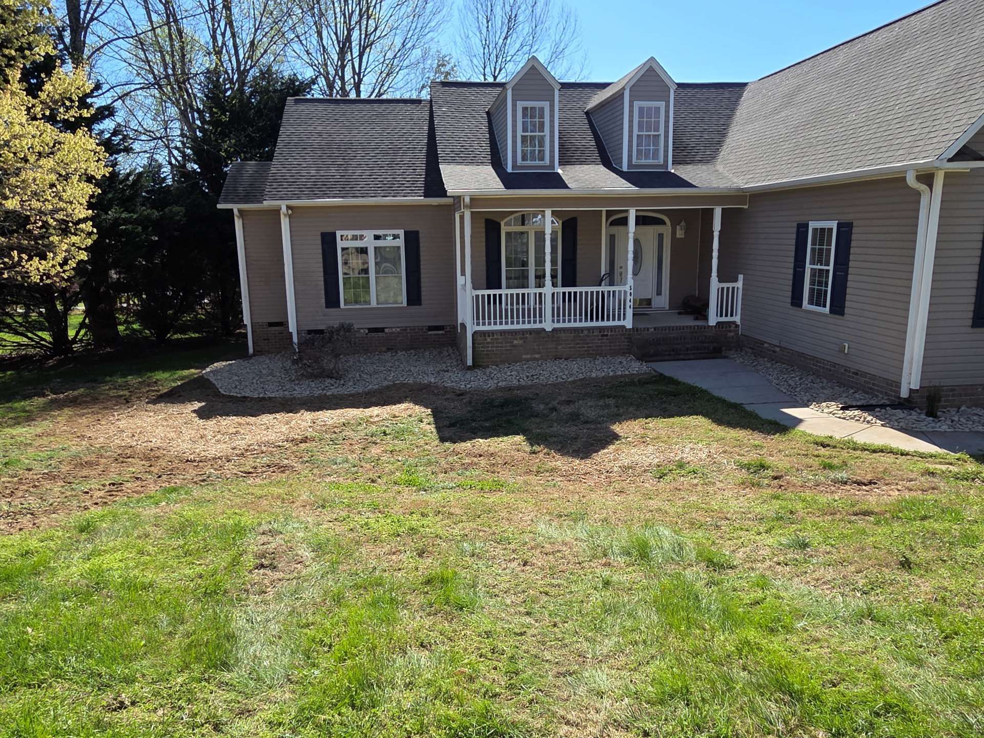 Suburban house with a front porch and dormer windows, shown from the front yard under a clear blue sky