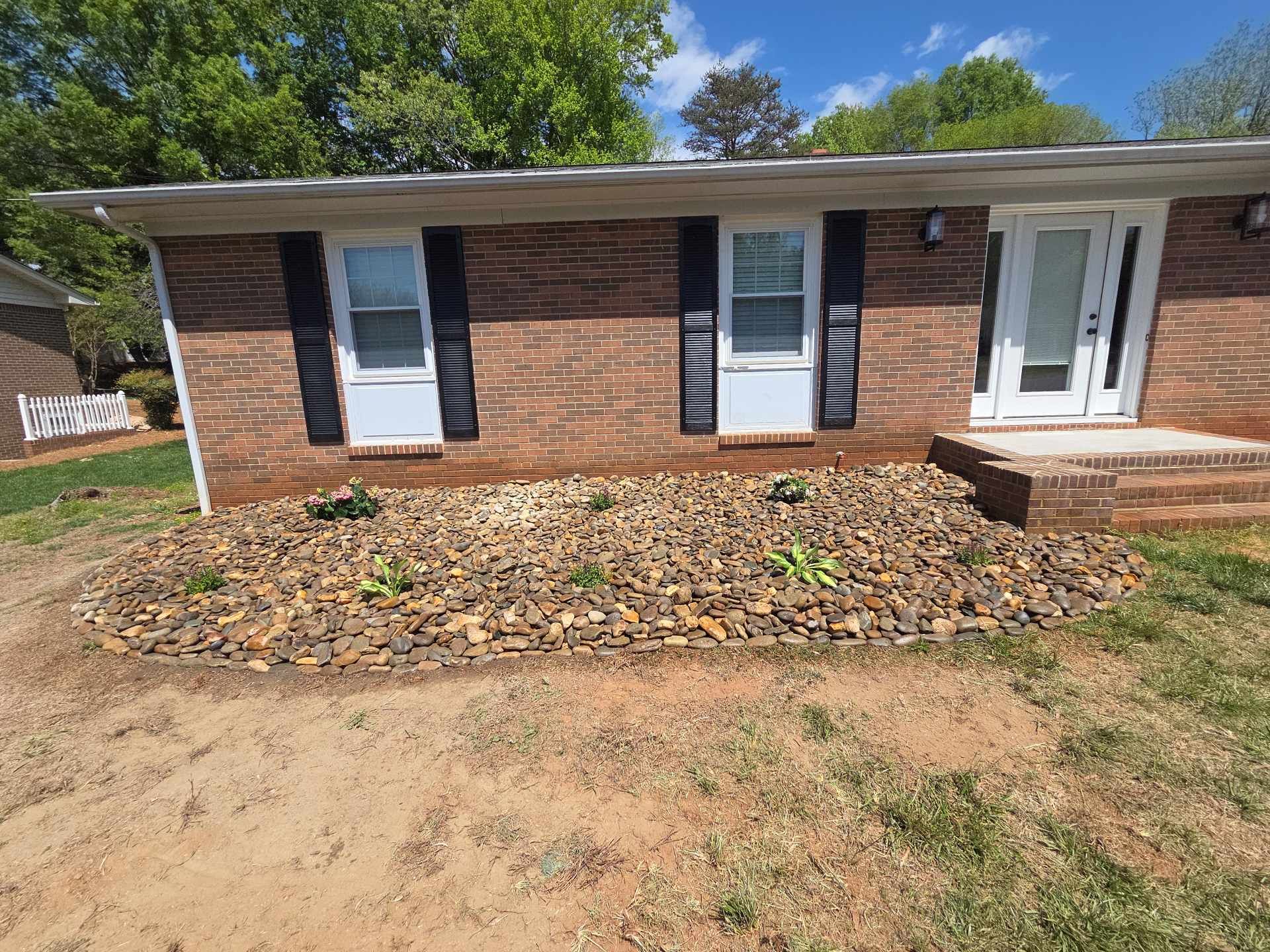 Single-story brick house with white shutters and front door, bare front yard, and a small porch.