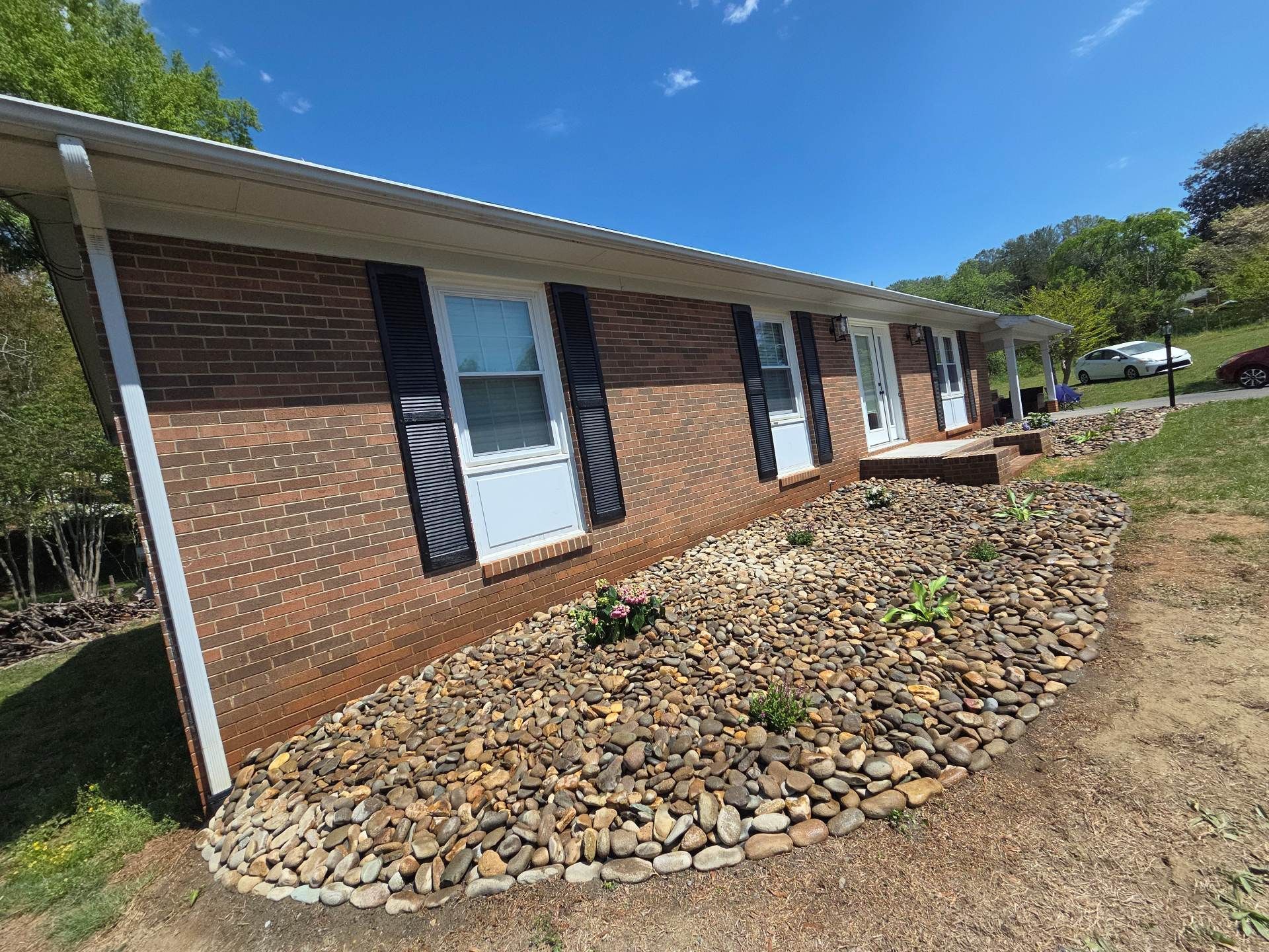Brick ranch house with white shutters and a rock-covered front bed under a blue sky