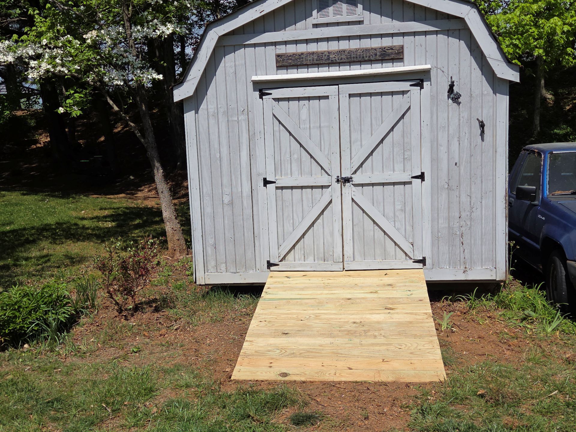 Gray shed with double doors and a wooden ramp in a grassy yard