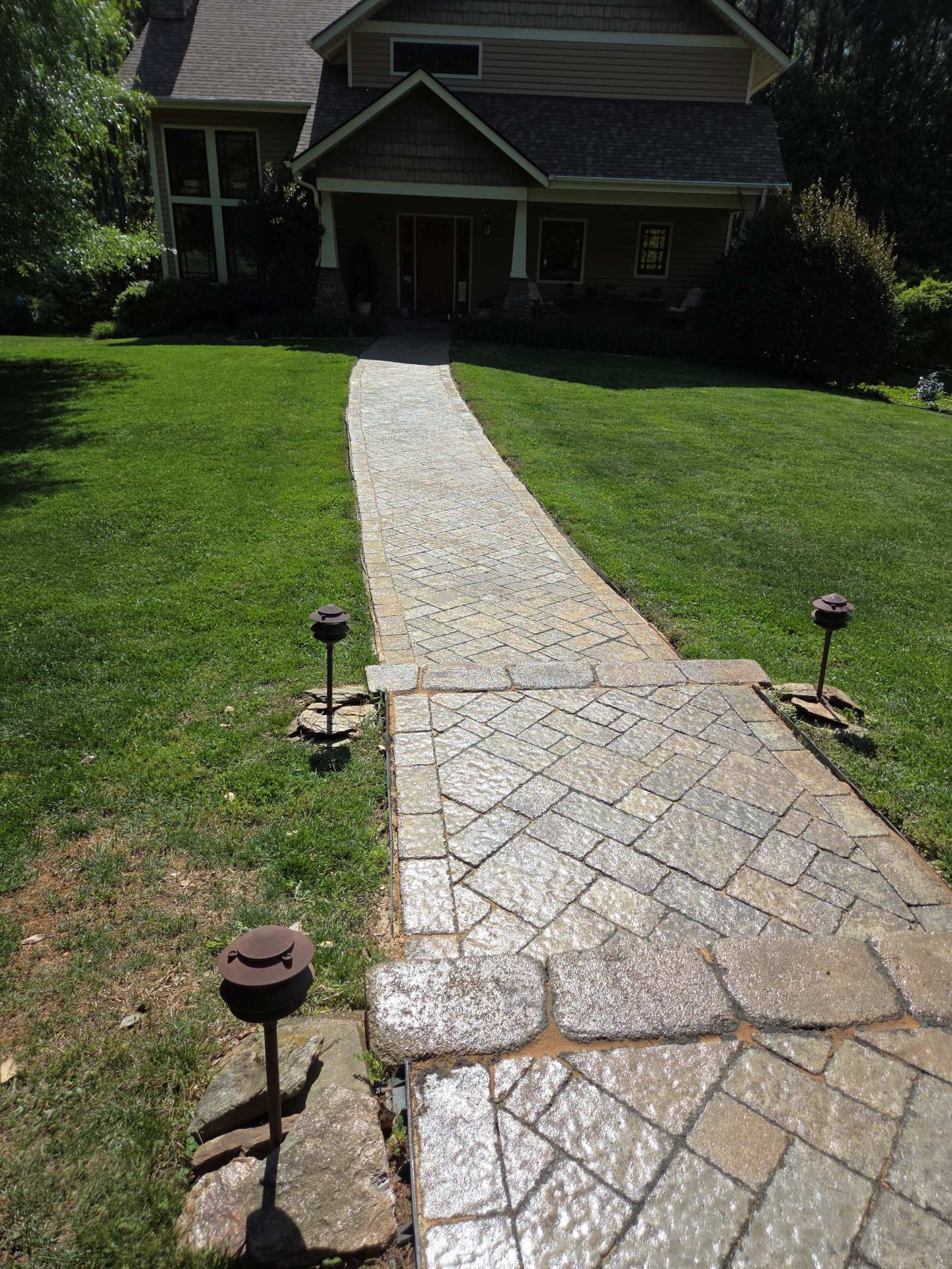 Curved stone walkway through green lawn leading to a dark house entrance