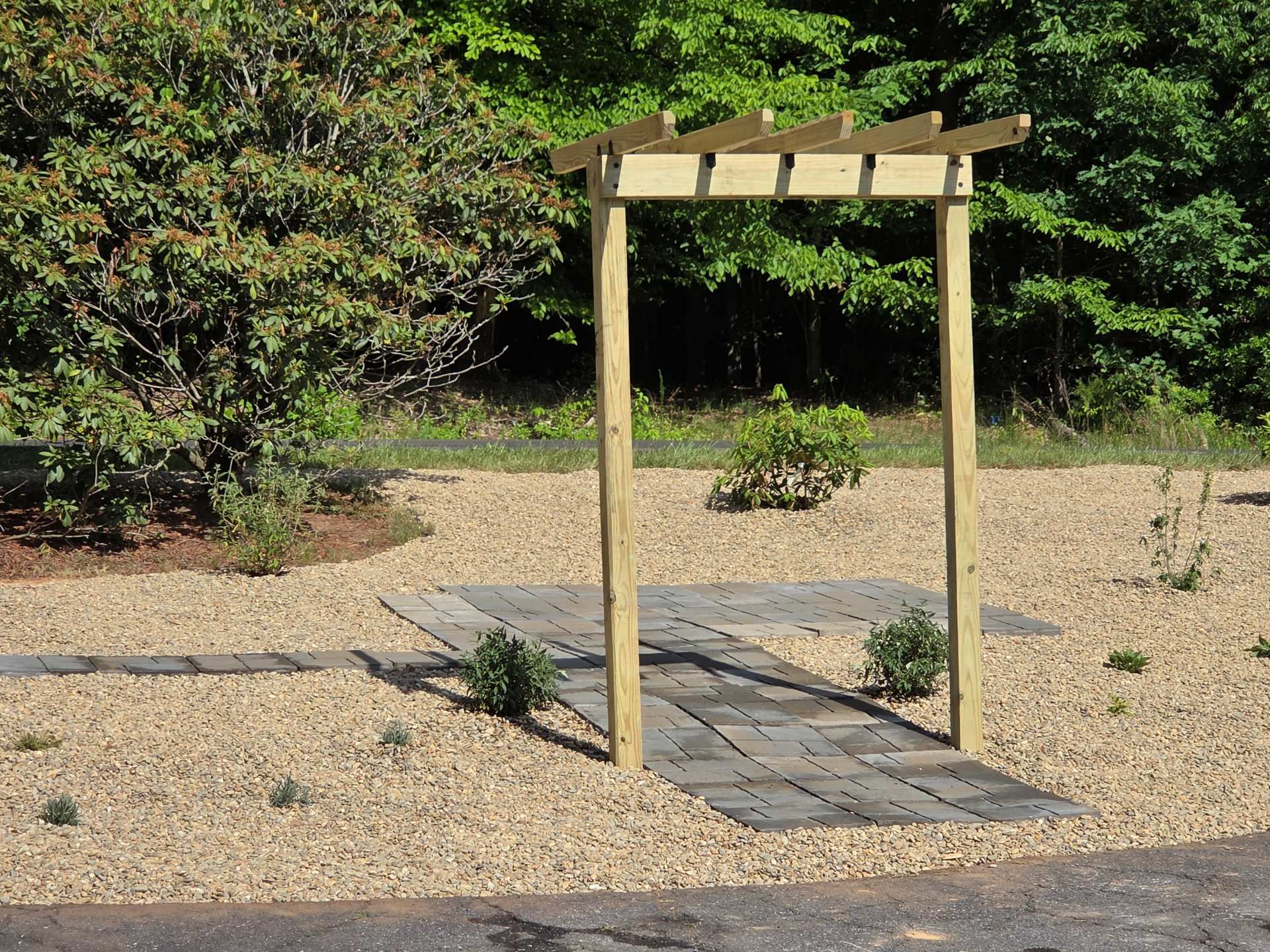Wooden pergola over a stone path in a gravel garden with shrubs and trees
