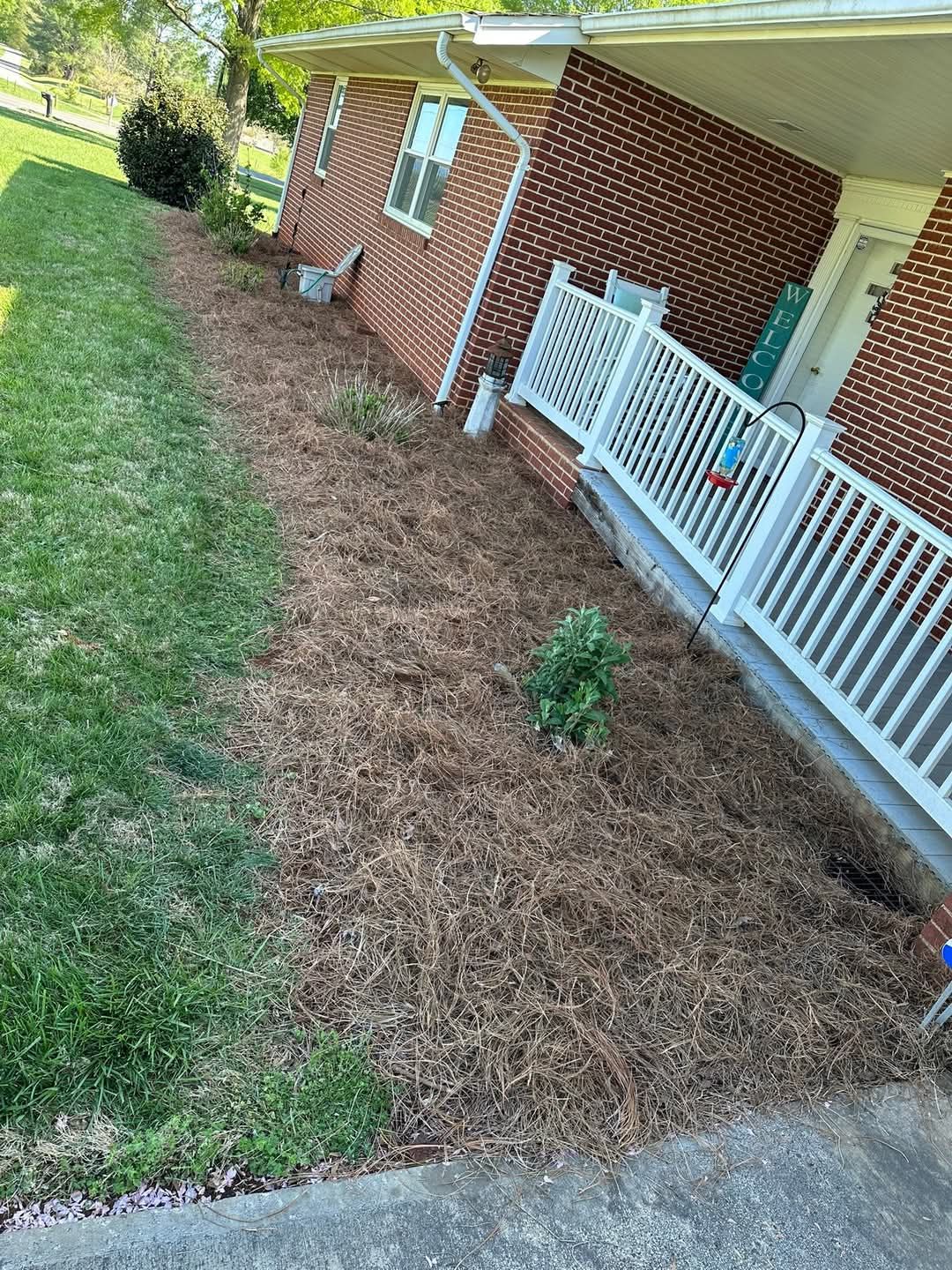 Brick house side yard with white fence, mulch bed, and a grassy lawn along the sidewalk.