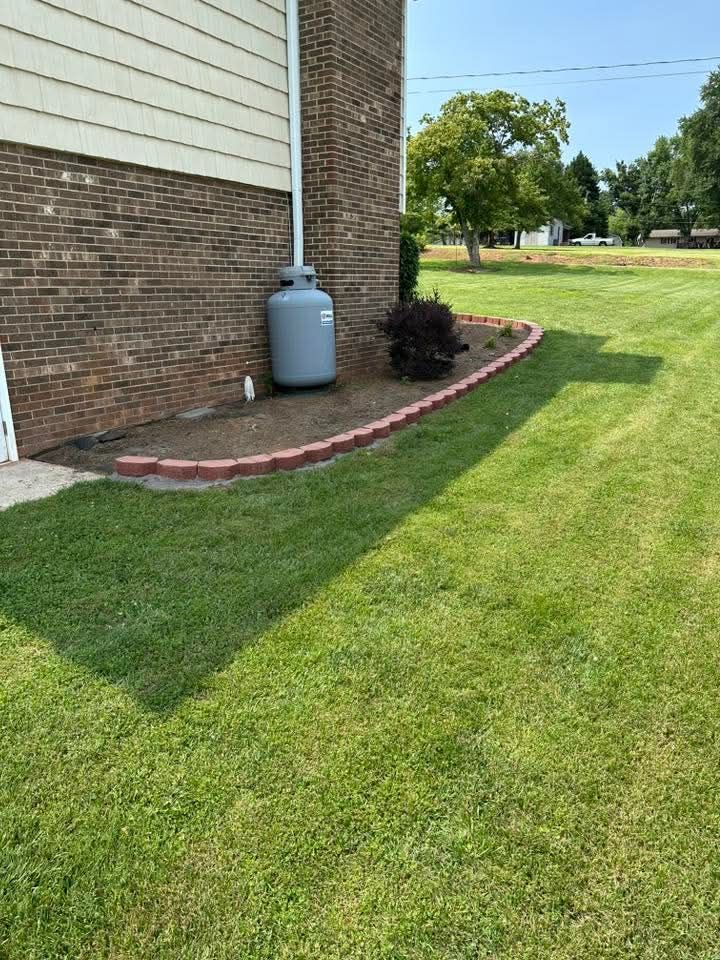 Brick house corner with propane tank, mulch border, and green lawn under sunny sky
