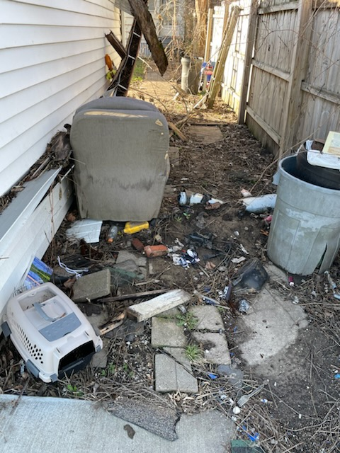 A dog crate is sitting in the dirt in front of a house.