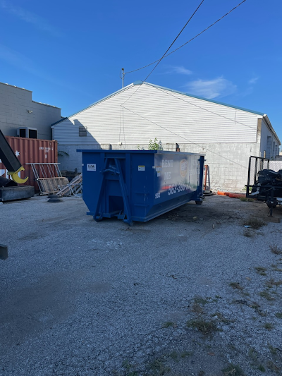 A large blue dumpster is parked in front of a white building.