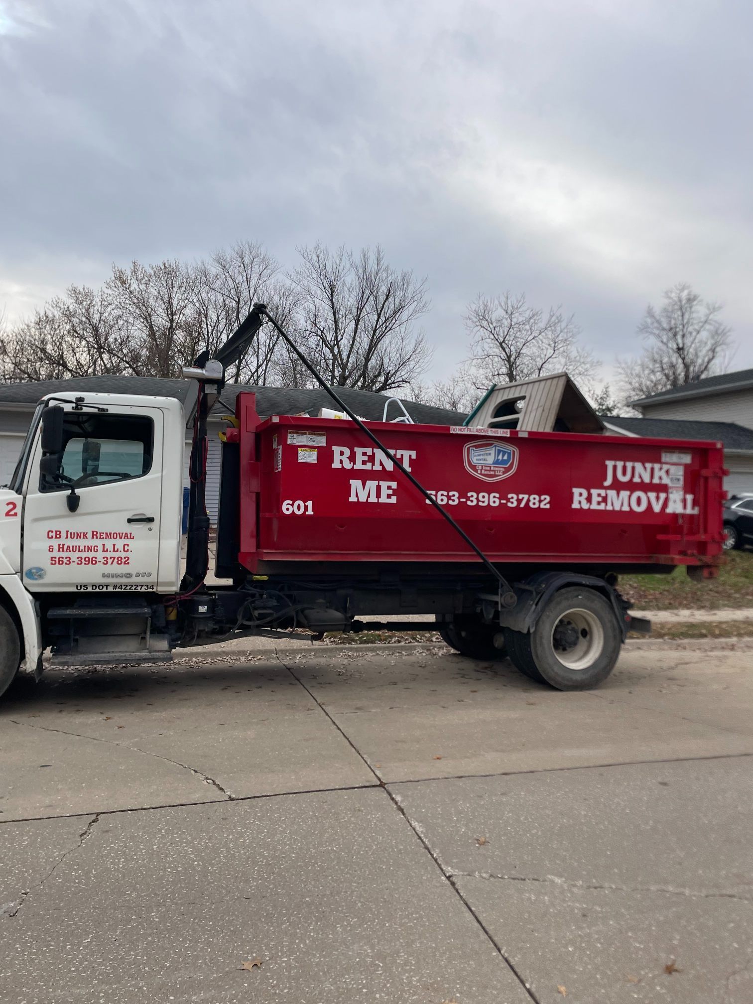 Red junk removal truck loaded with debris parked on a street.