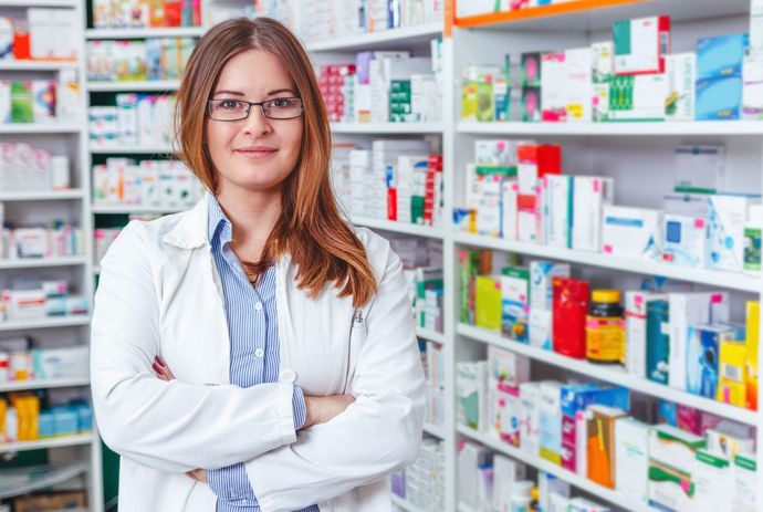 Cheerful female pharmacist standing by rows of medicine.