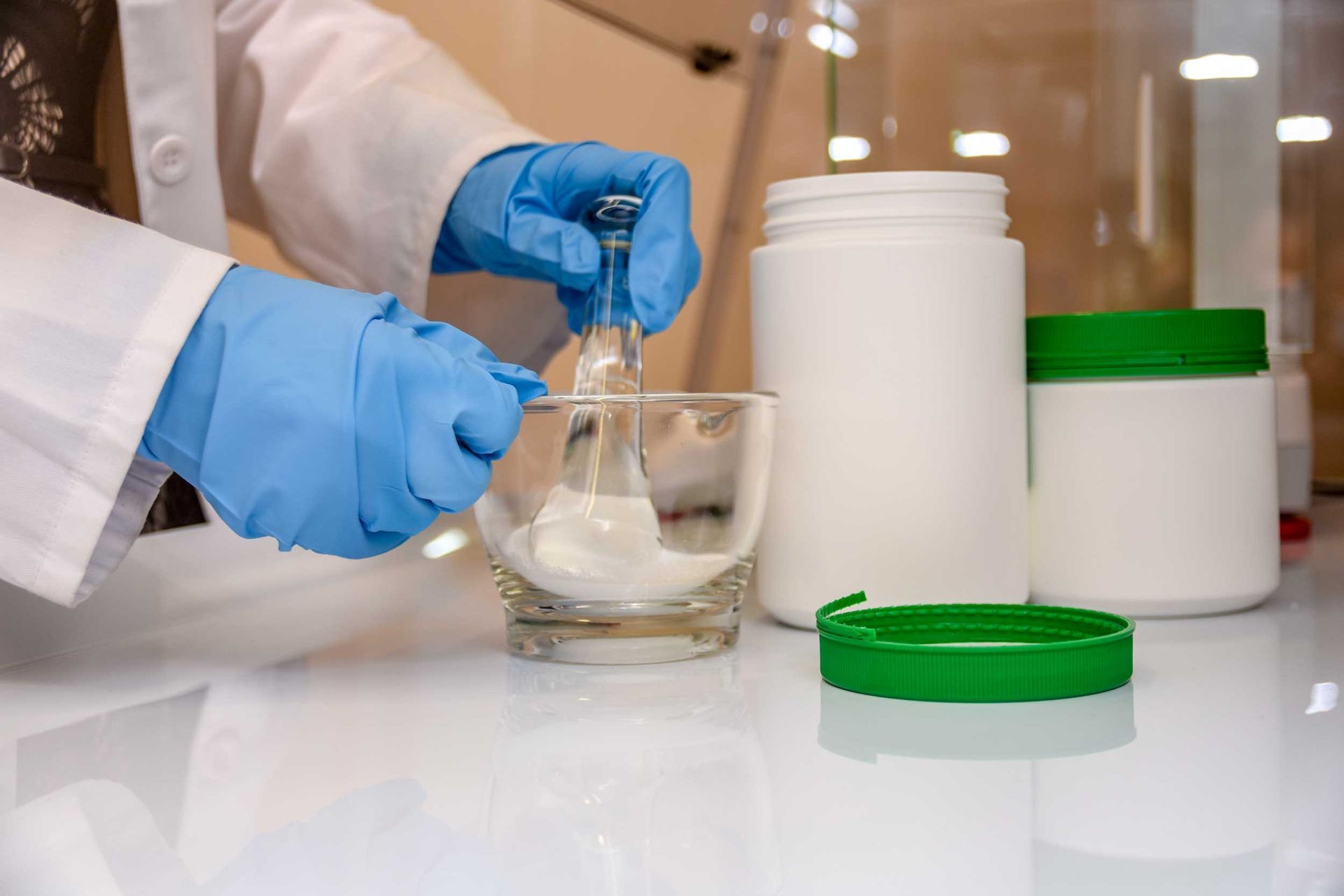 A pharmacist in blue gloves performing medication compounding.
